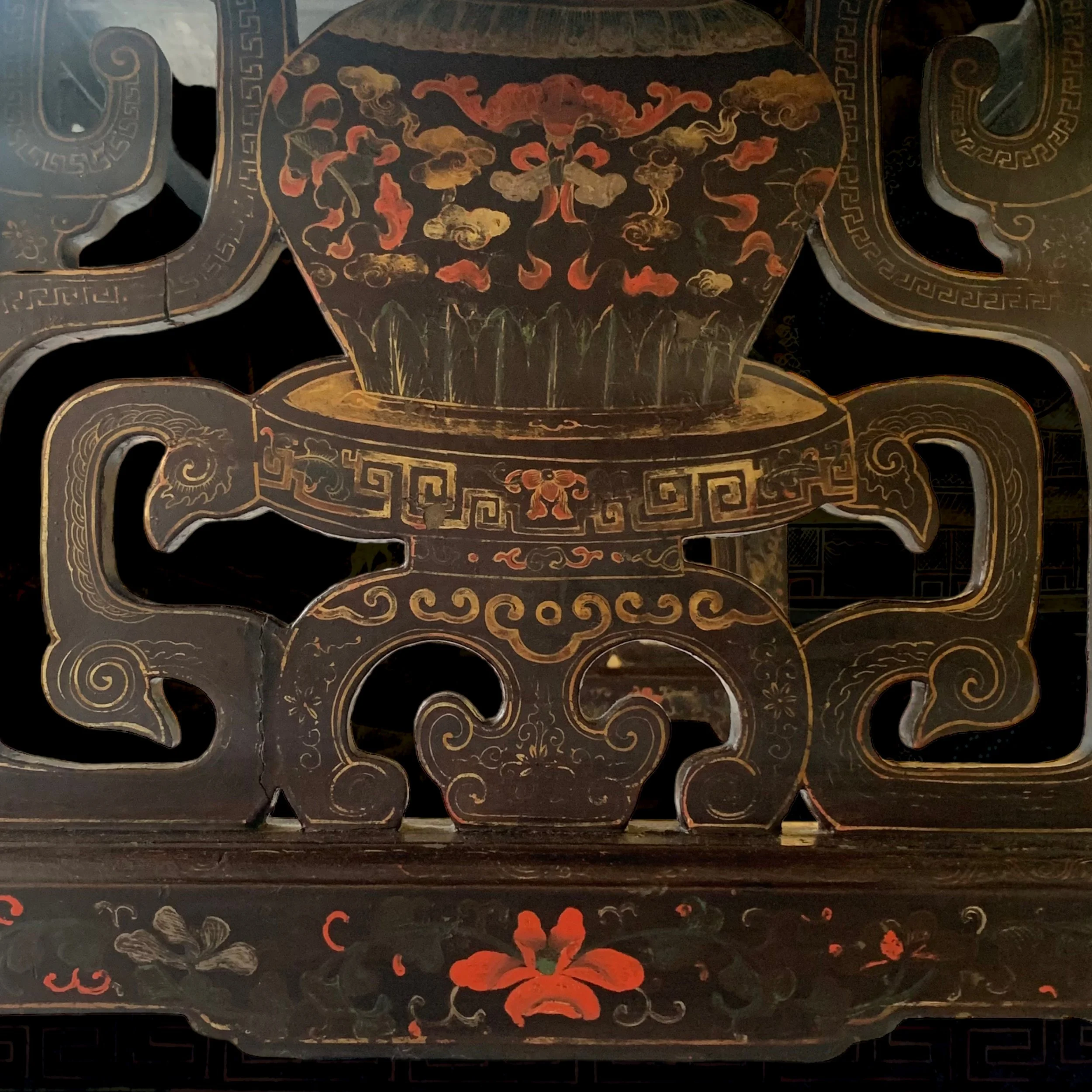 Close-up of a black lacquered Asian-style decorative screen with gold and red floral and cloud patterns. The design features a large vase with swirling handles and a red flower at the bottom center.
