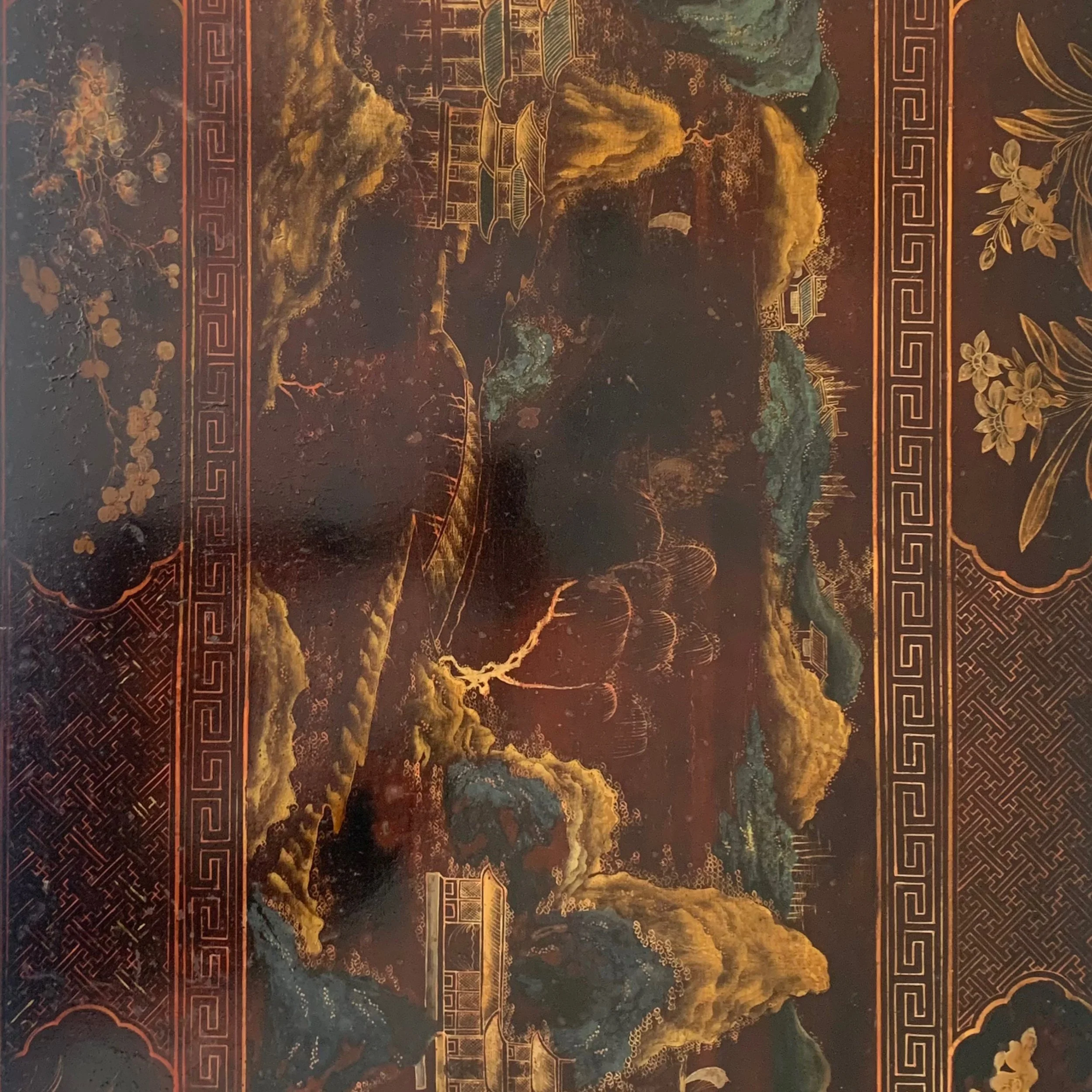 A traditional Chinese landscape painting with mountains, trees, and buildings in gold, orange, and green tones, bordered by intricate geometric patterns.