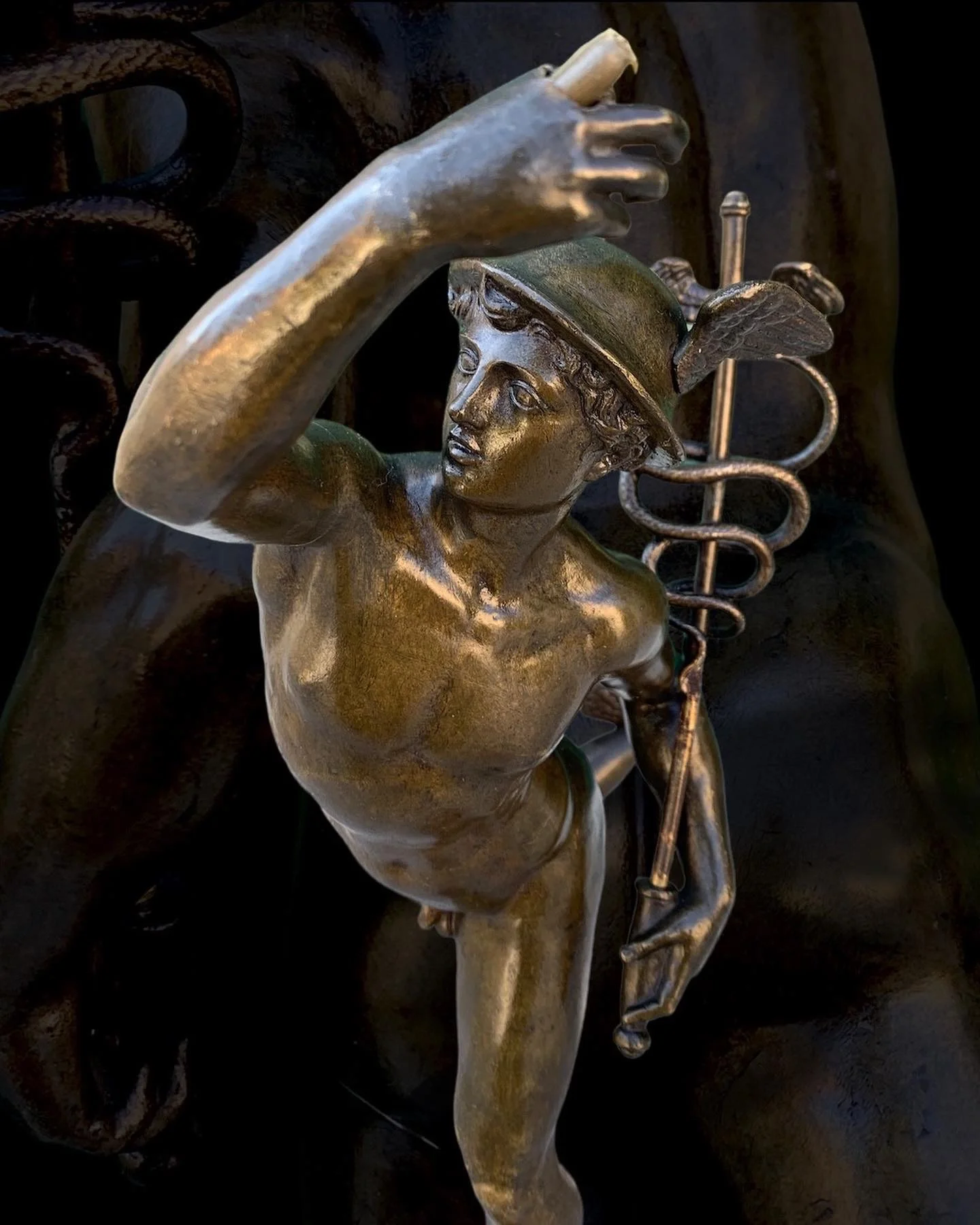 A bronze sculpture of a young boy with a helmet and wings, holding a staff, with a caduceus symbol in the background.