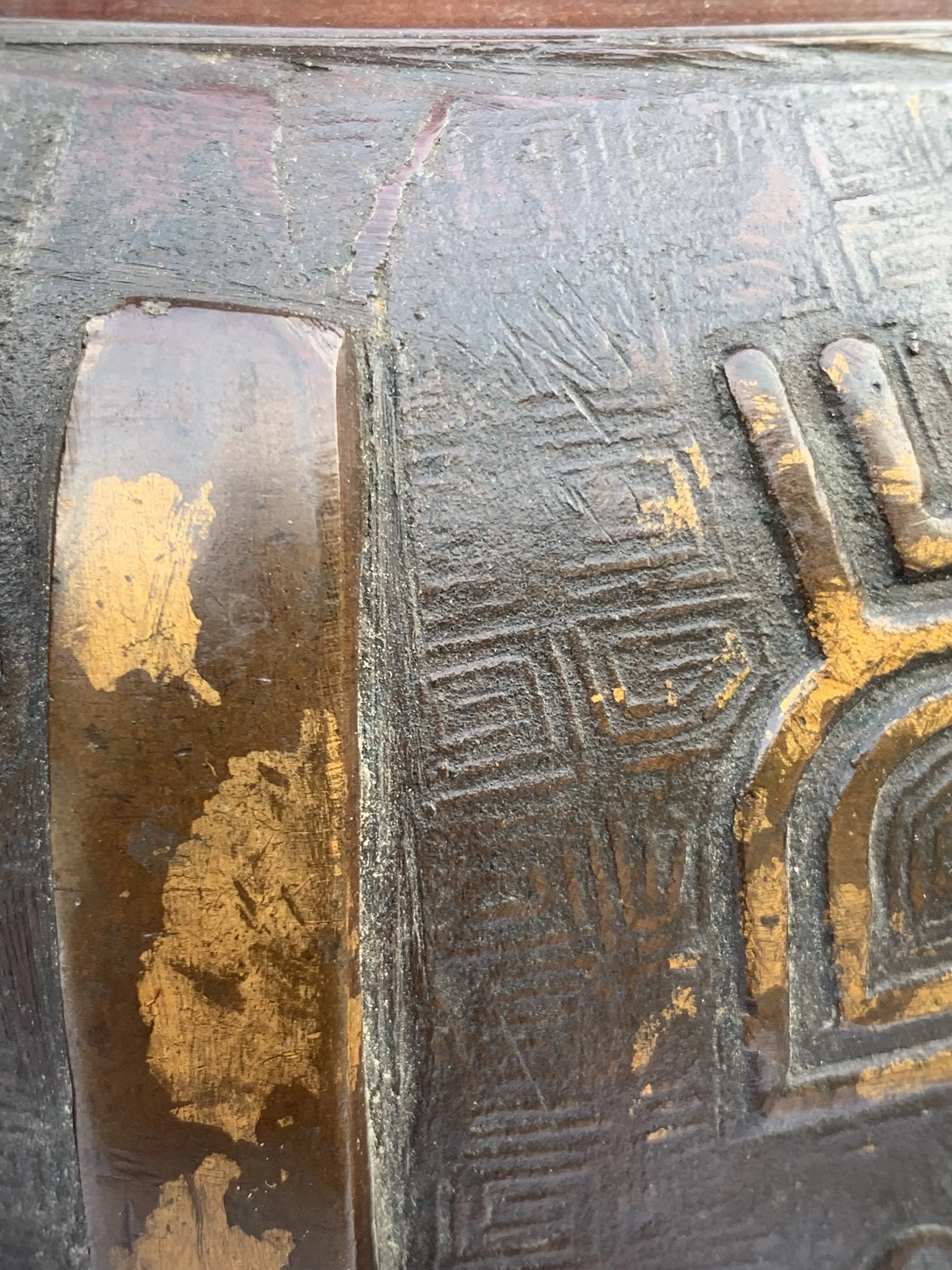 Close-up of a weathered bronze or metal surface with an aged patina and engraved geometric patterns.