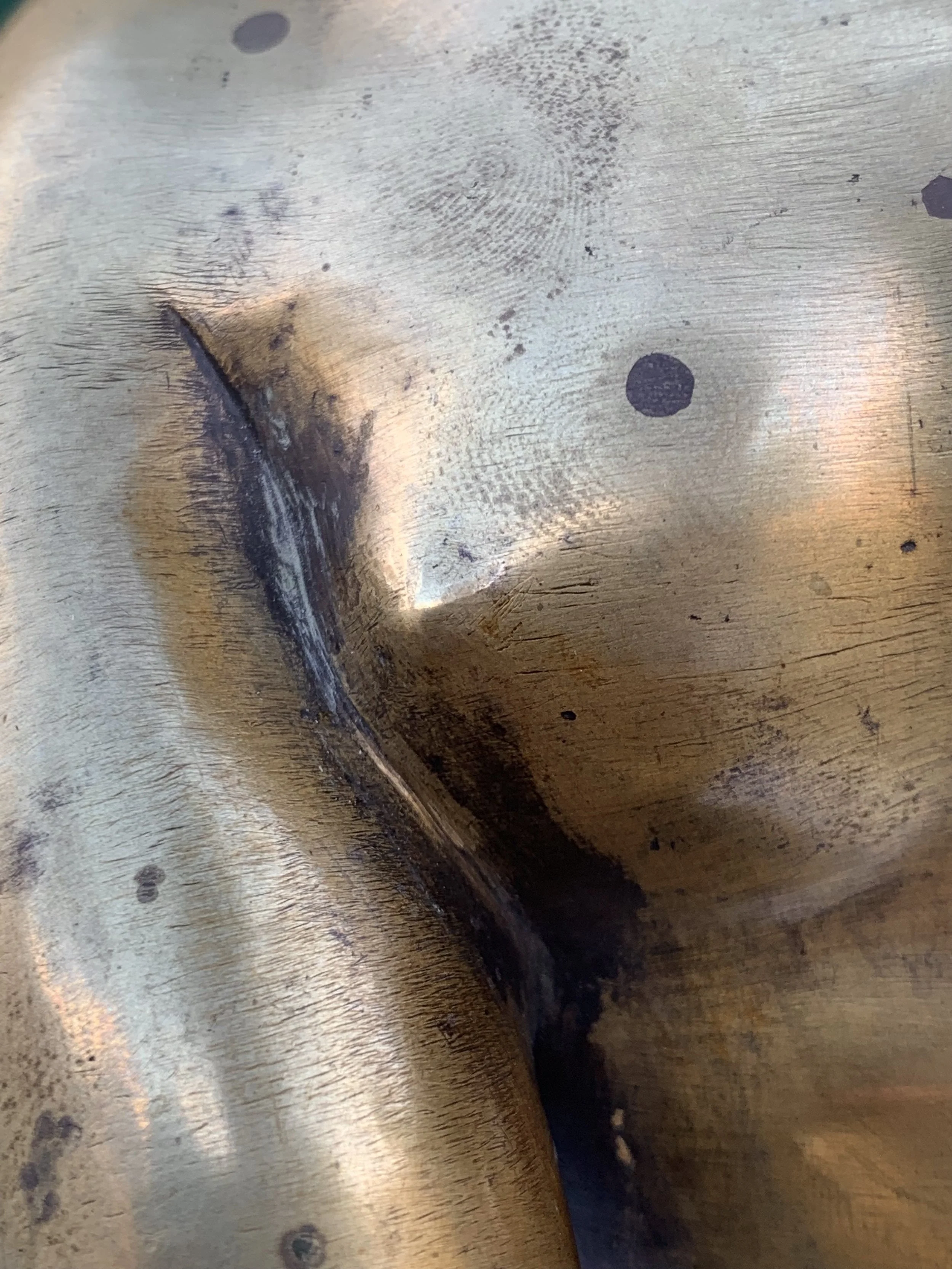 Close-up of a worn, damaged metallic surface with scratches, burn marks, and a curved edge.