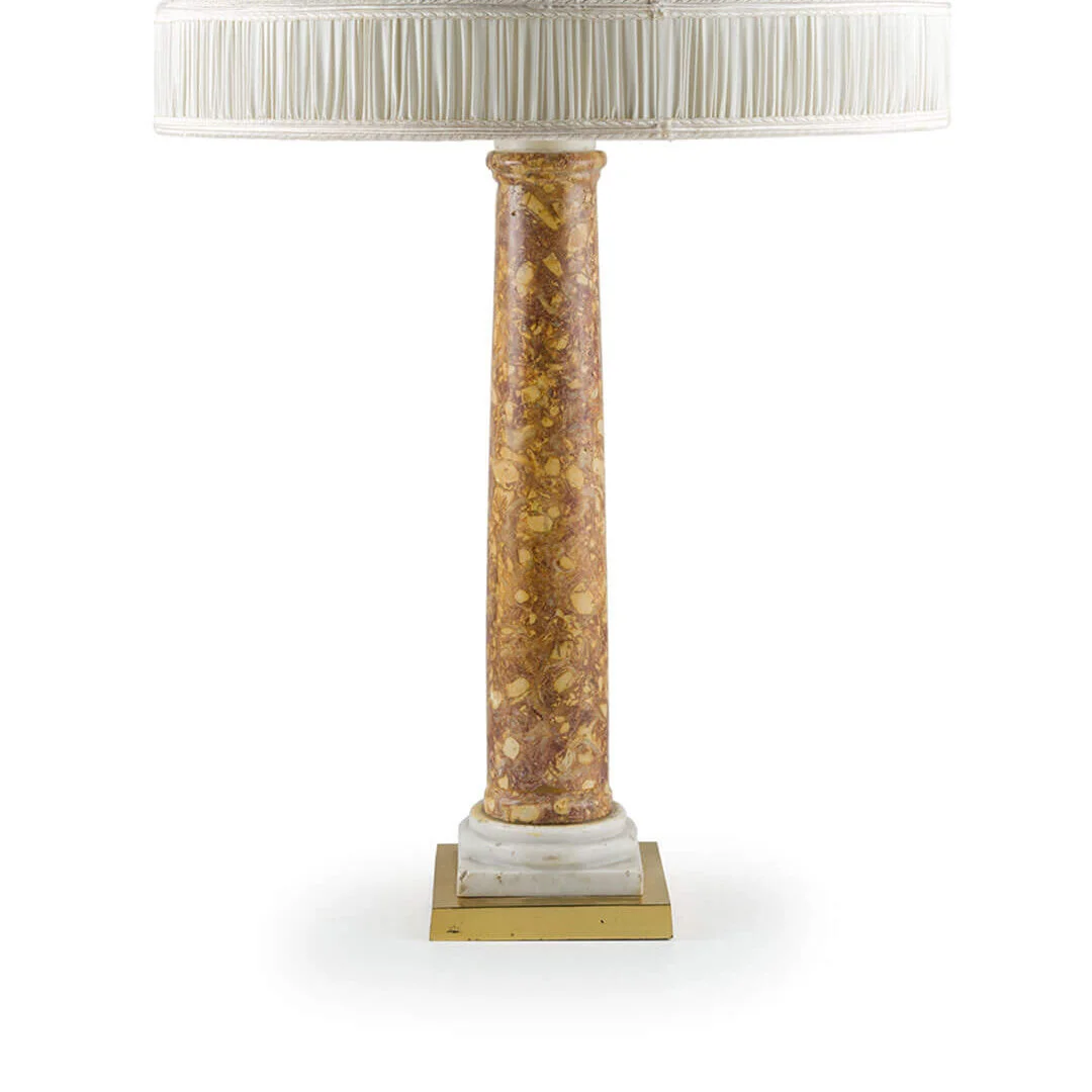 A decorative table lamp with a tall, cylindrical marble-like base in shades of brown and gold, topped with a white, pleated lampshade.