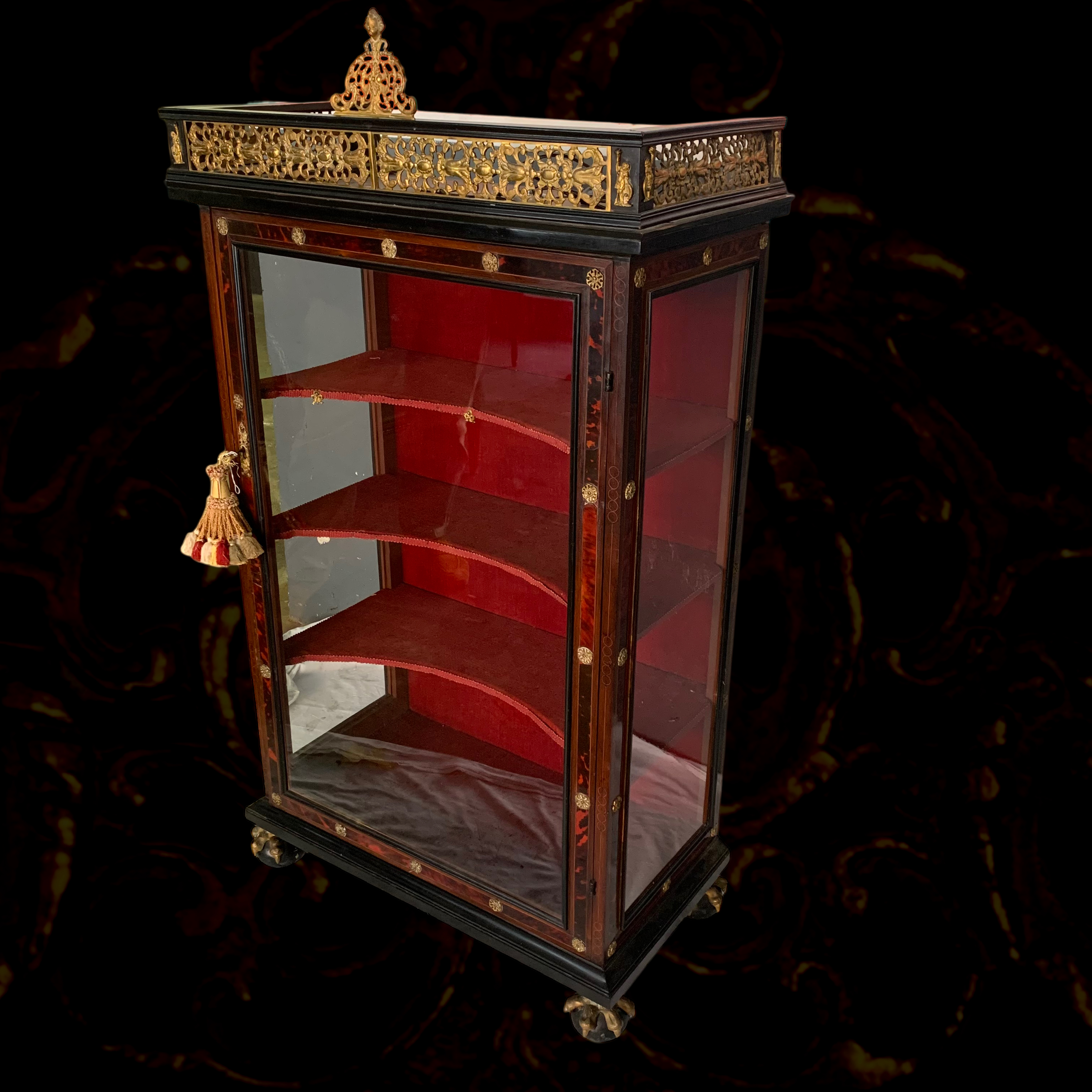 An antique display cabinet with glass sides and a red interior, decorated with gold accents and a crown on top.