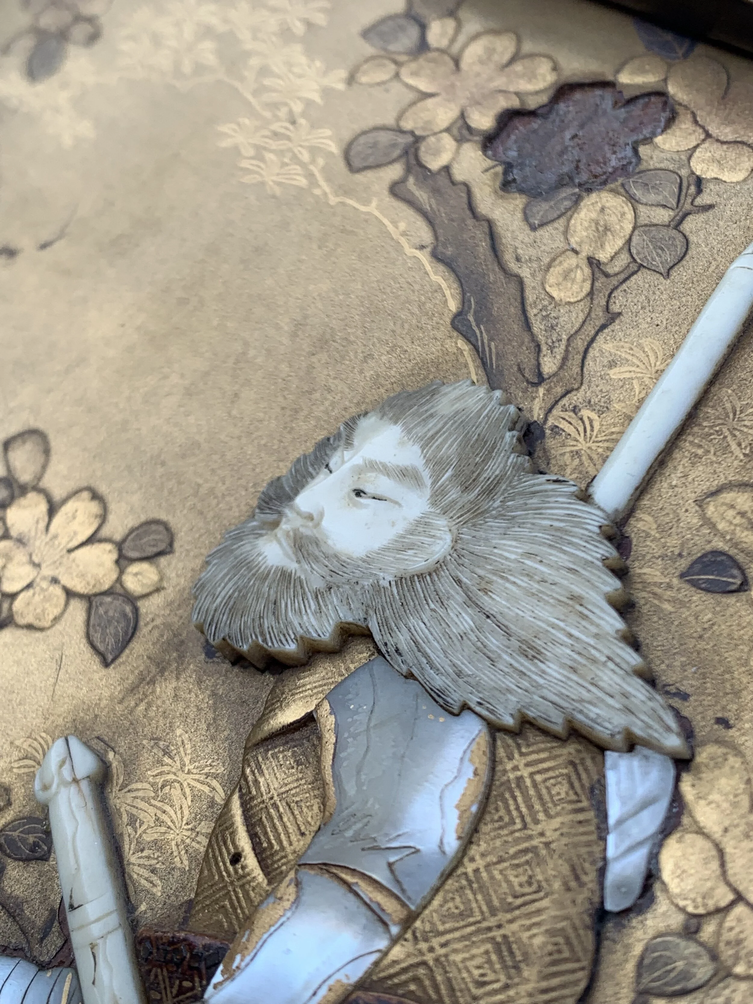 Close-up view of a decorative metal image of a face with flowing hair on an ornate, golden-brown background with floral patterns.