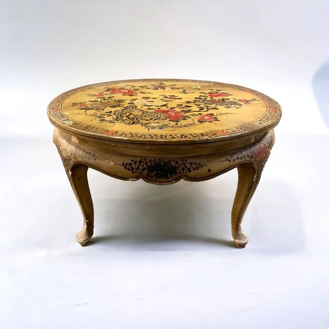 Vintage round wooden table with floral design on the top surface and carved legs.