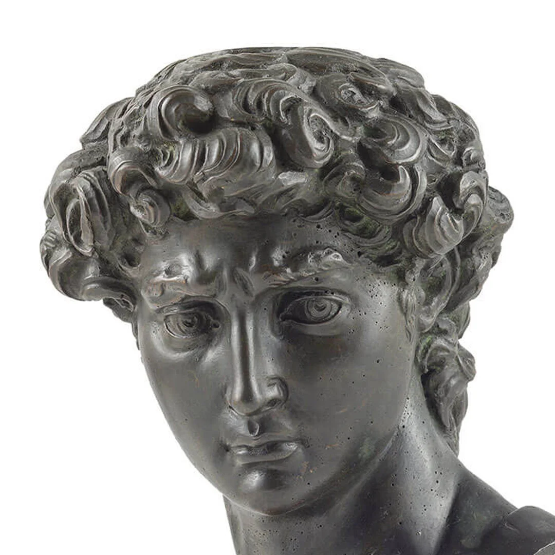 Close-up of a dark metal sculpture of a woman's face with detailed curly hair and a serious expression.