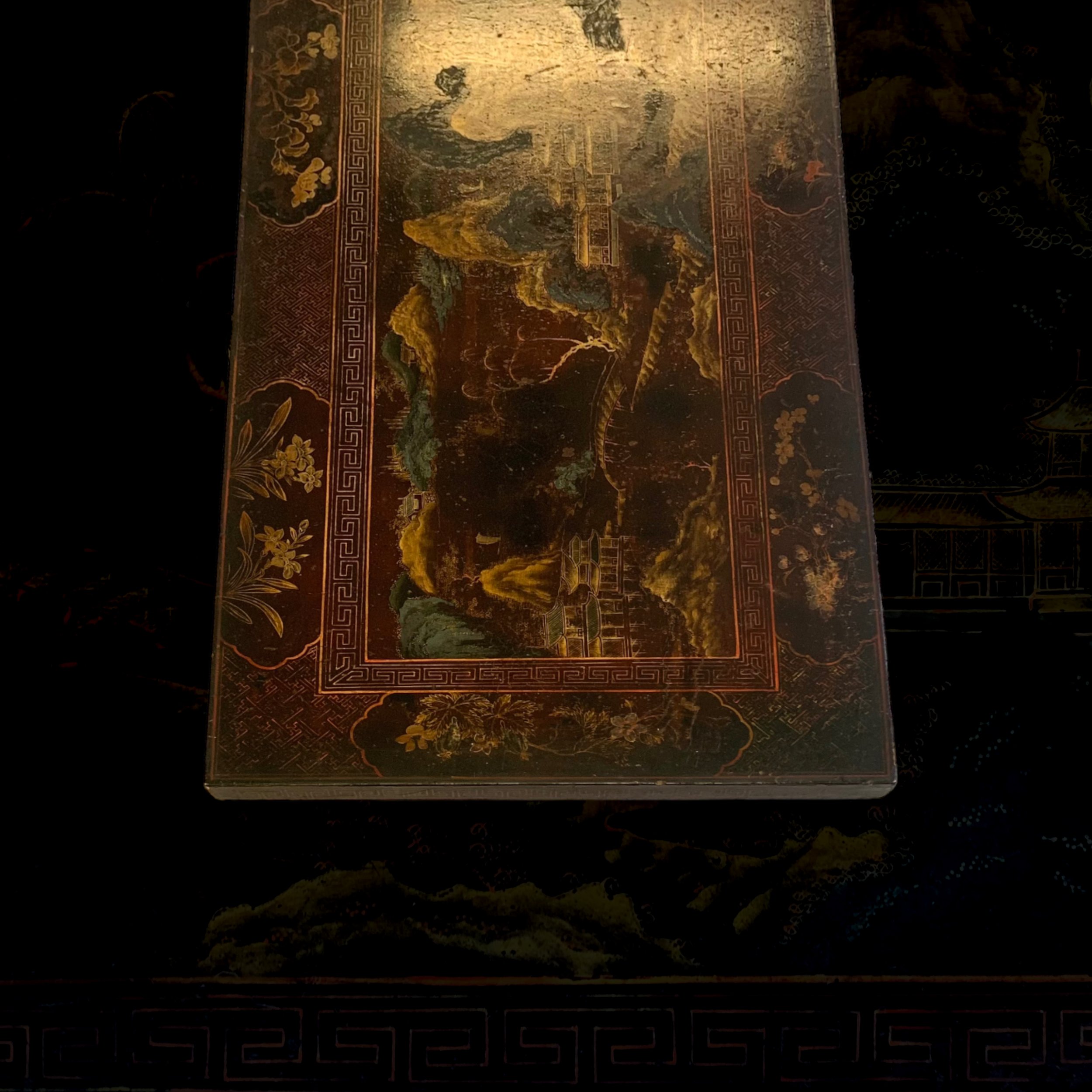 A rectangular decorative box with a traditional Asian landscape painting on the lid, featuring mountains, trees, buildings, and clouds in gold, green, and red tones.