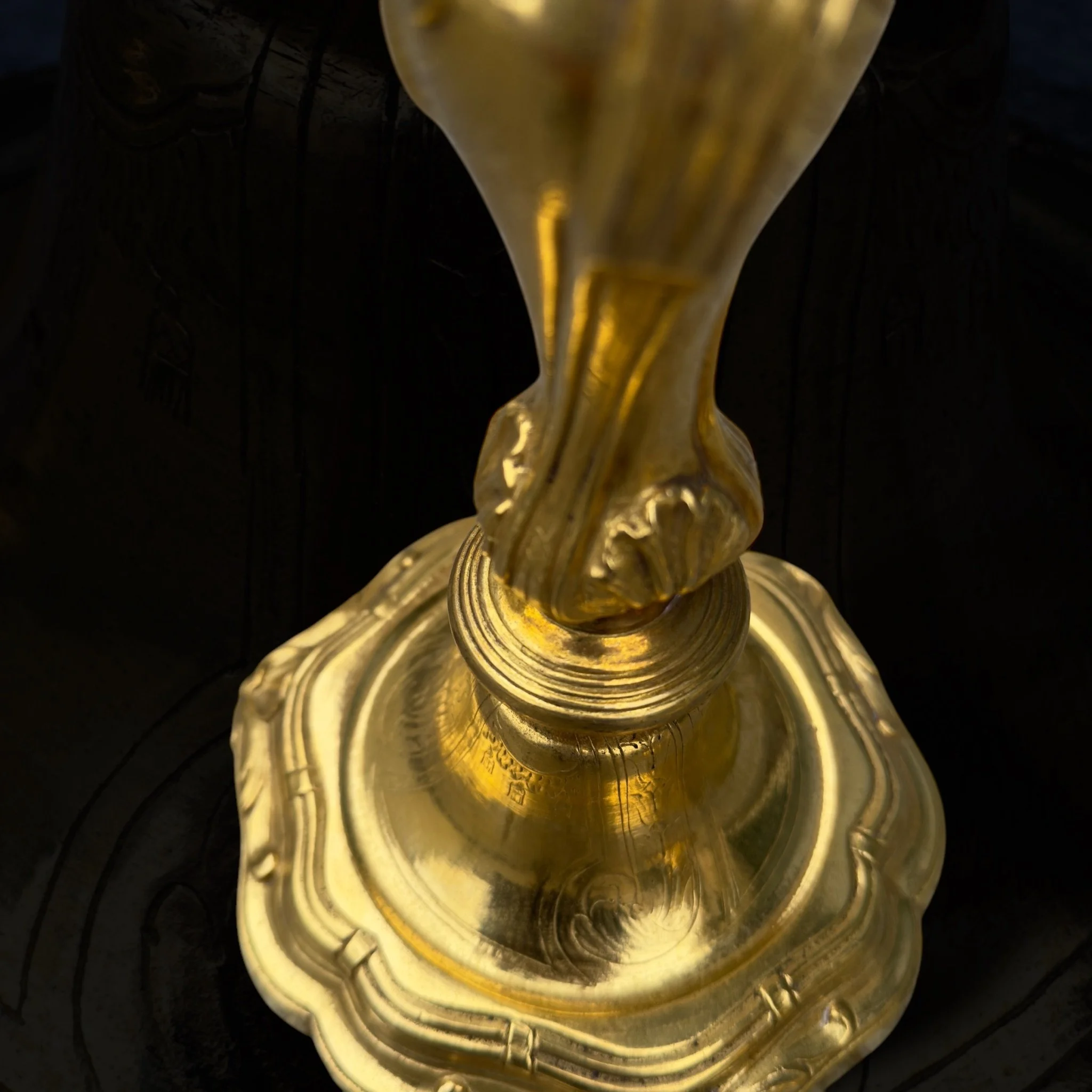 Close-up of a gold-colored ornate object, viewed from above, with a black textured background.