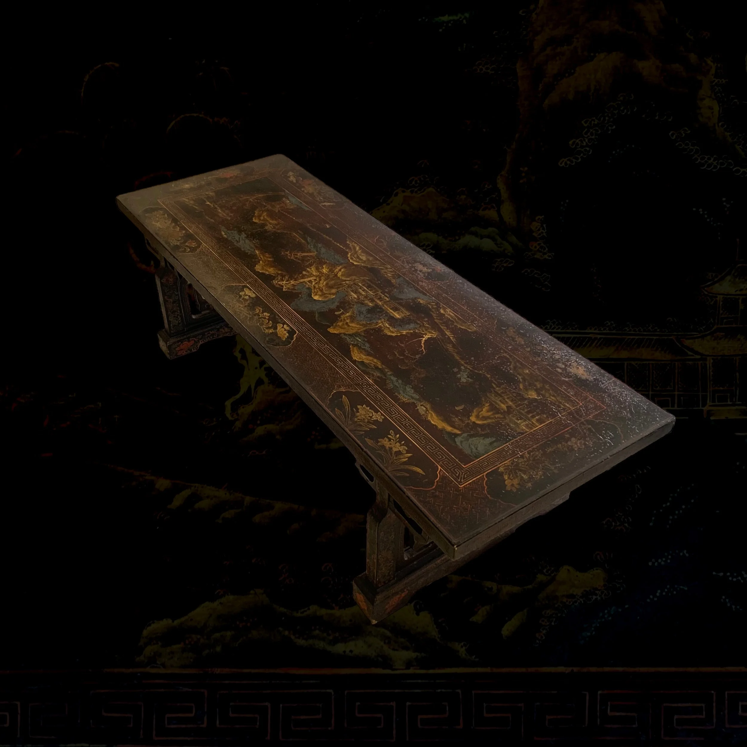An ornately decorated rectangular table with intricate Chinese landscape scene painted on its surface, supported by carved wooden legs.