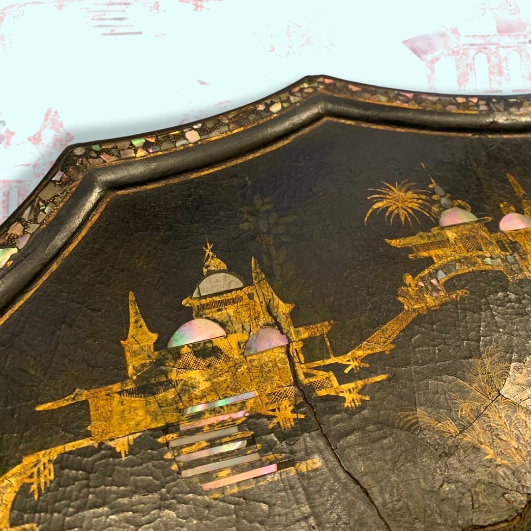 Close-up of a black decorative item with gold-embossed castle, palm trees, and dome structures, featuring iridescent accents and a crack running through it.