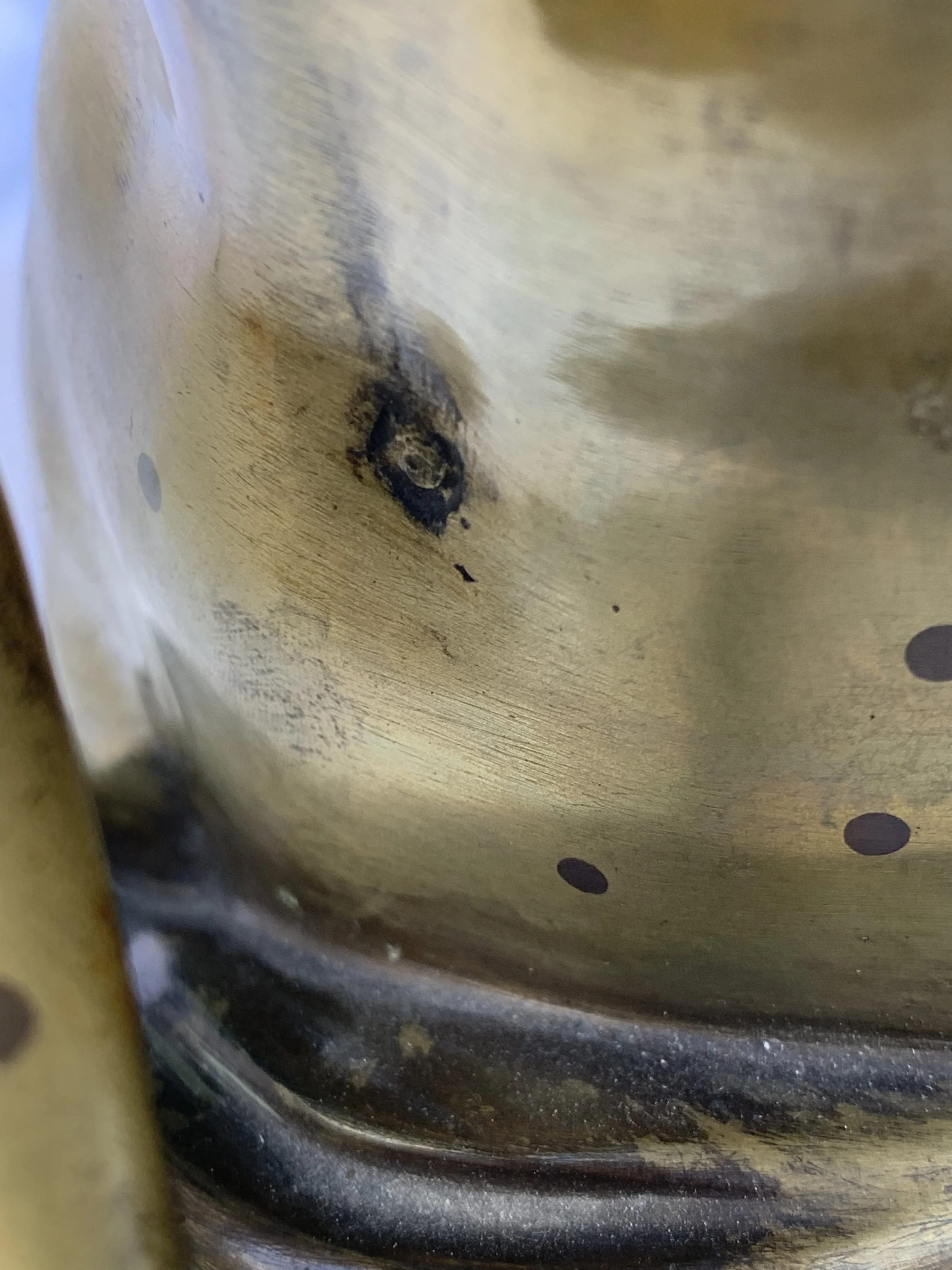 Close-up of a metallic surface with a burn mark and small black spots, possibly on a frying pan or a similar cooking utensil.