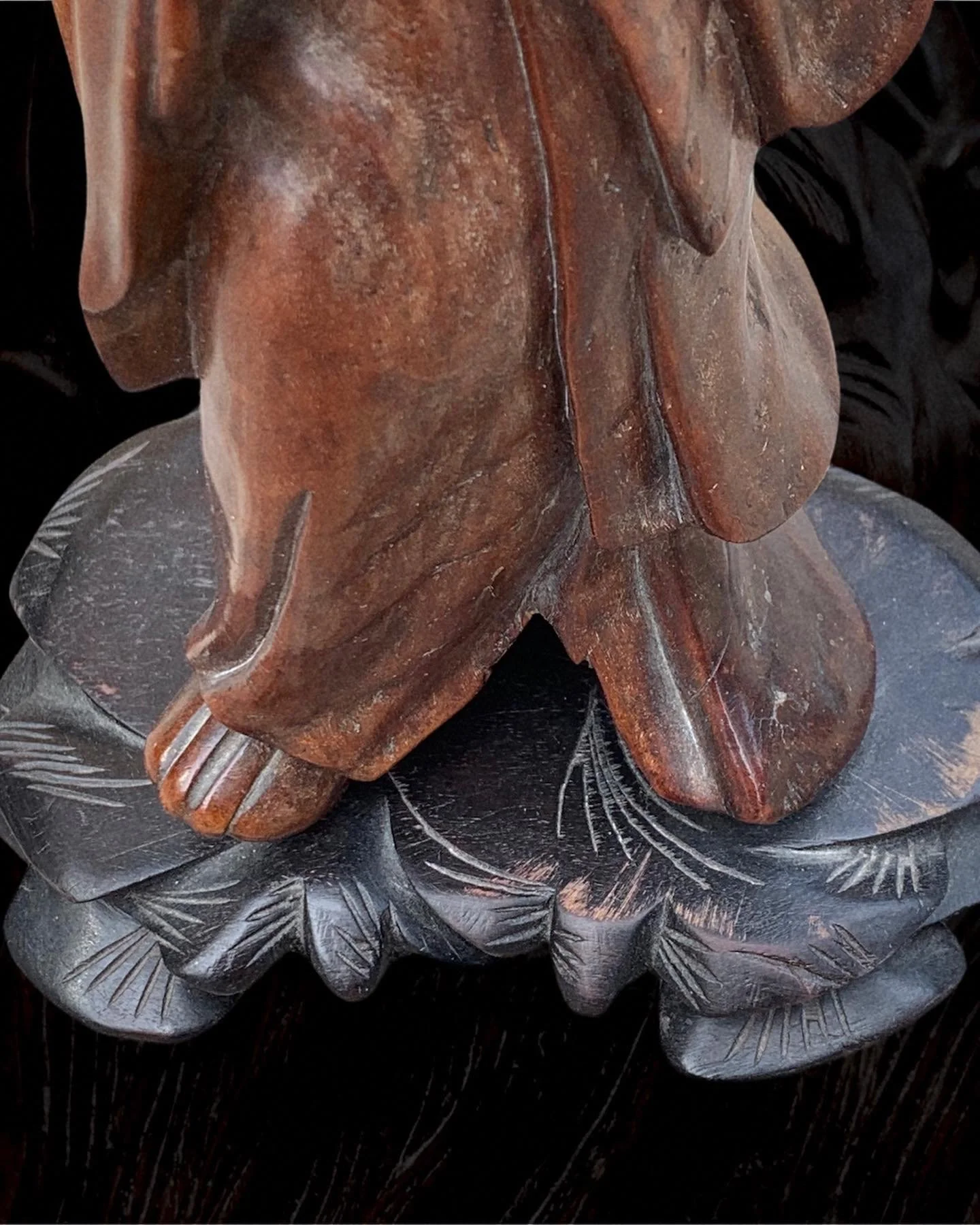 Close-up of a carved wooden figure standing on an intricately carved wooden base.