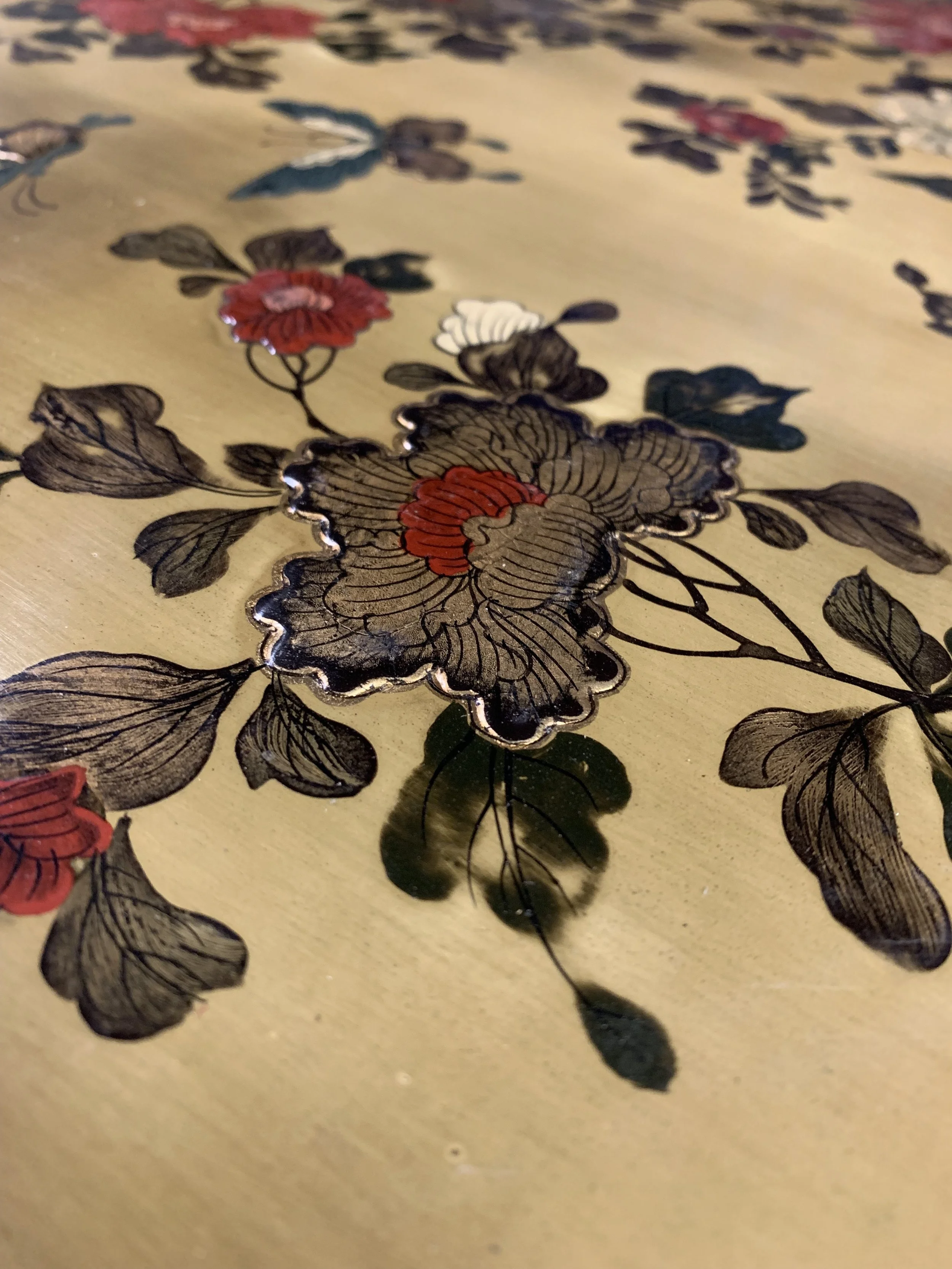 Close-up of a decorative floral design on a golden surface, featuring black, red, and white flowers with detailed line work and a metallic outline.