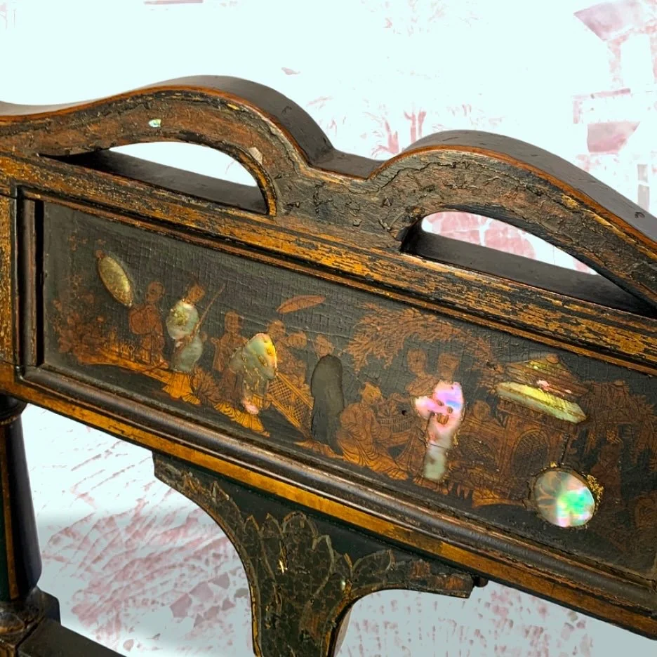 Close-up of an antique wooden piece with a detailed painted and inlaid scene depicting a traditional social gathering, possibly of Asian origin, featuring multiple figures in historical attire.
