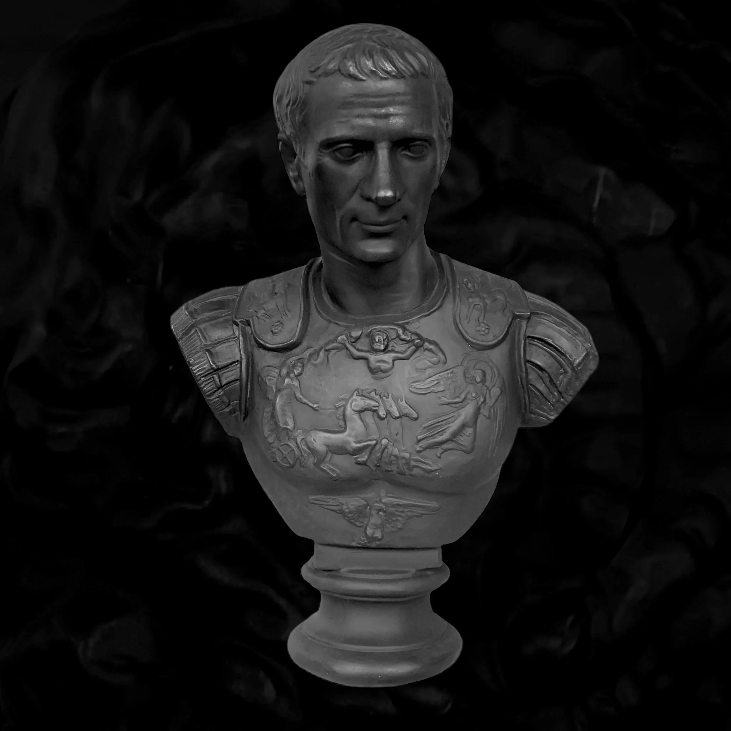 Black and white bust sculpture of a man in ancient Roman military armor with detailed bas-reliefs on the chest, set against a dark background.