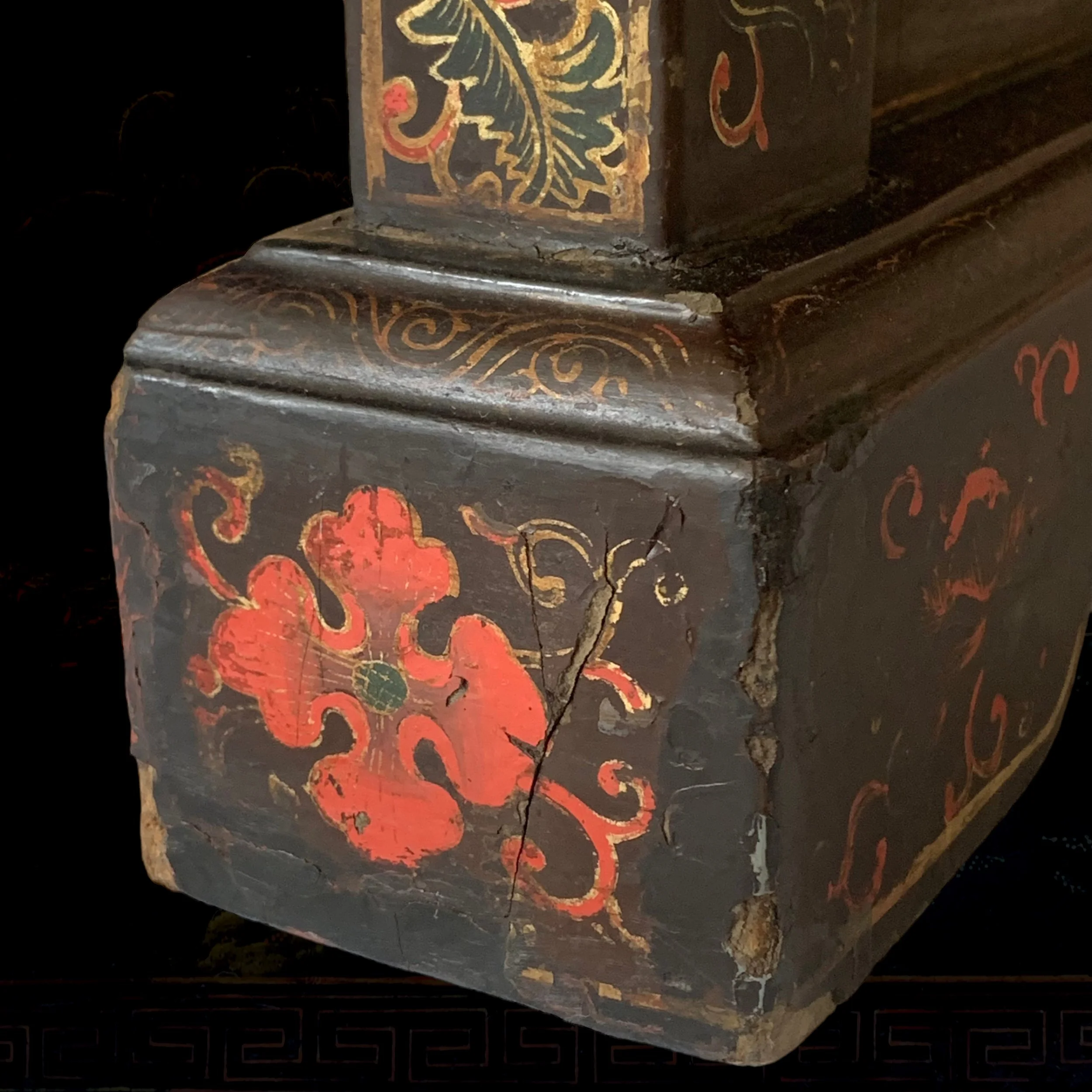 Close-up of a decorated, old wooden furniture piece with a red floral and vine pattern and visible cracks and chipped paint.