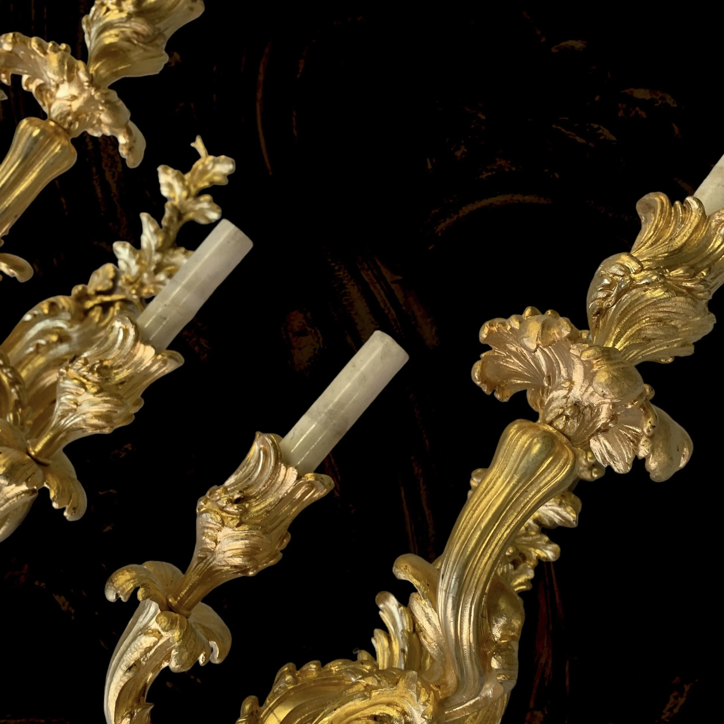 Close-up of a ornate gold chandelier with detailed leaf and scroll designs against a dark background.