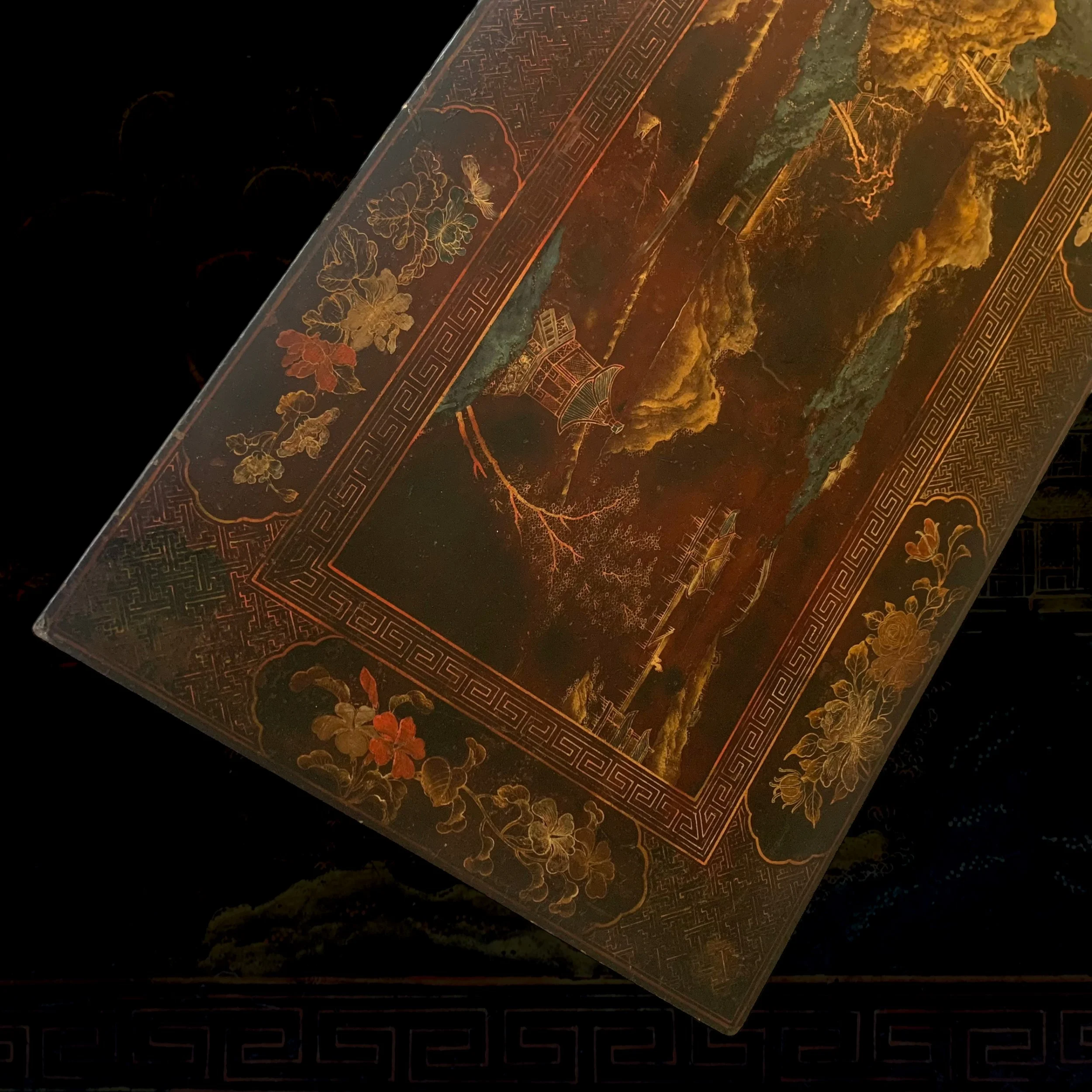 Close-up of an ornate, decorative box with intricate gold floral patterns and traditional Chinese landscape artwork, featuring mountains, water, and buildings.