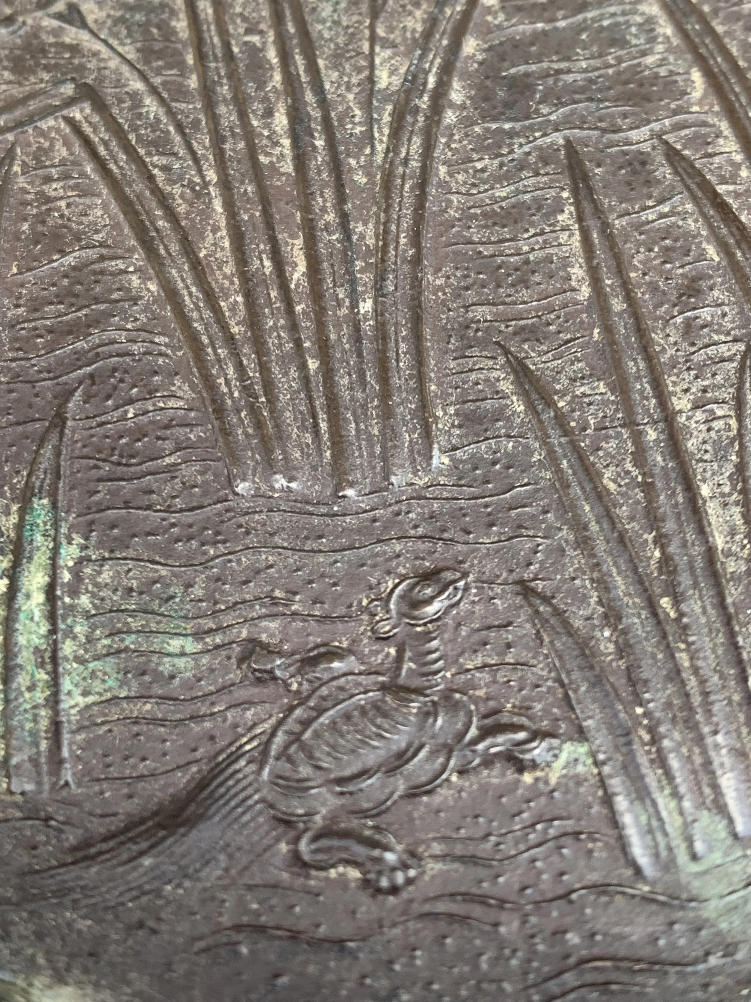 Close-up of a metal surface with an engraved image of a duck, water, and tall grass or reeds.