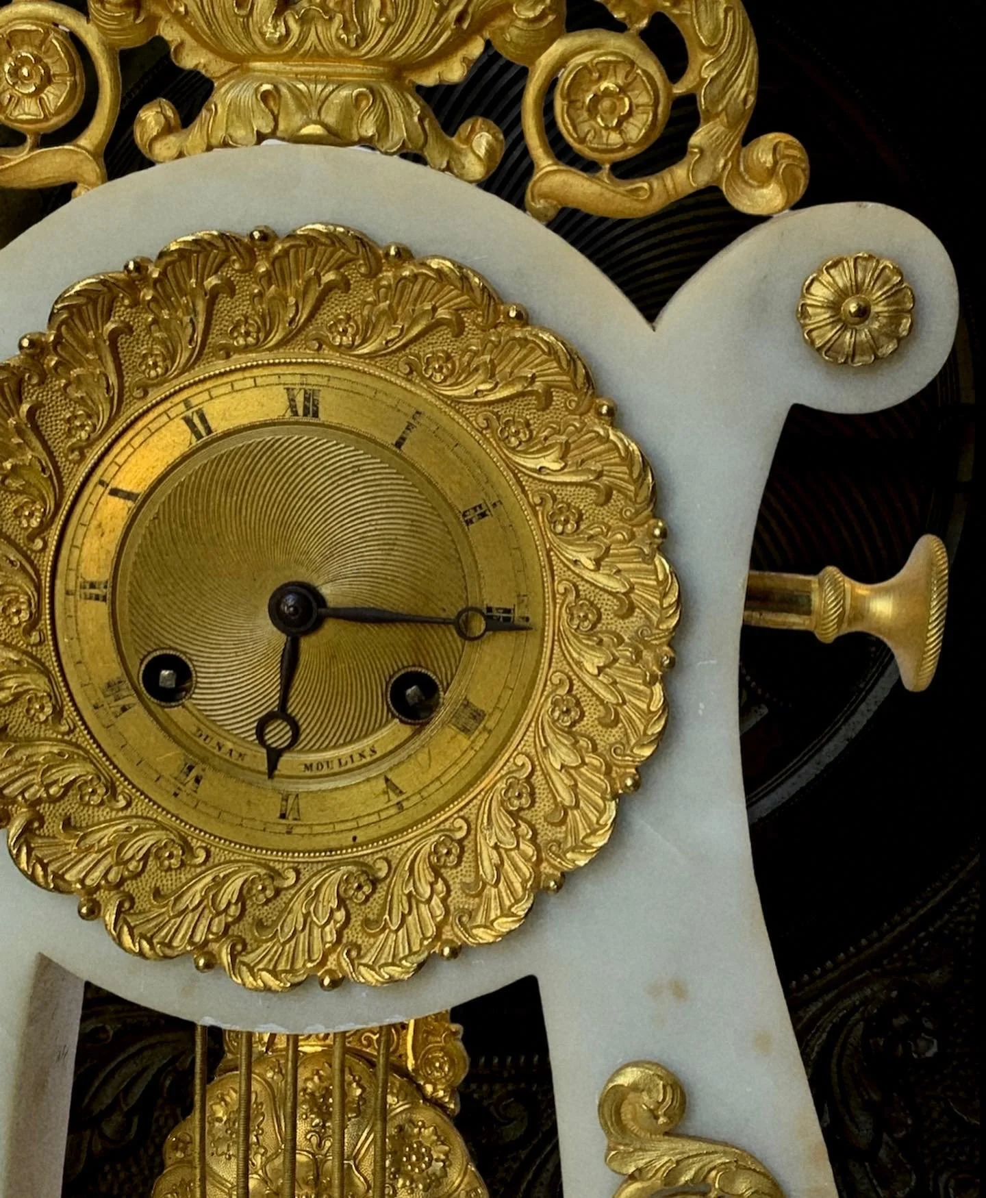Close-up of an ornate antique clock with gold embellishments and Roman numerals.