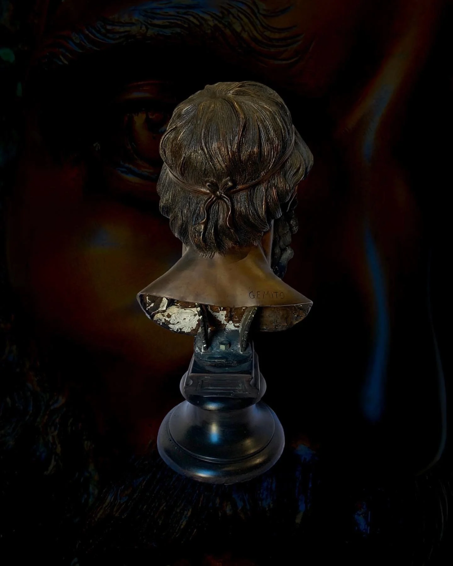 Bronze bust of a man with long hair, mounted on a black pedestal, with an abstract colorful background.