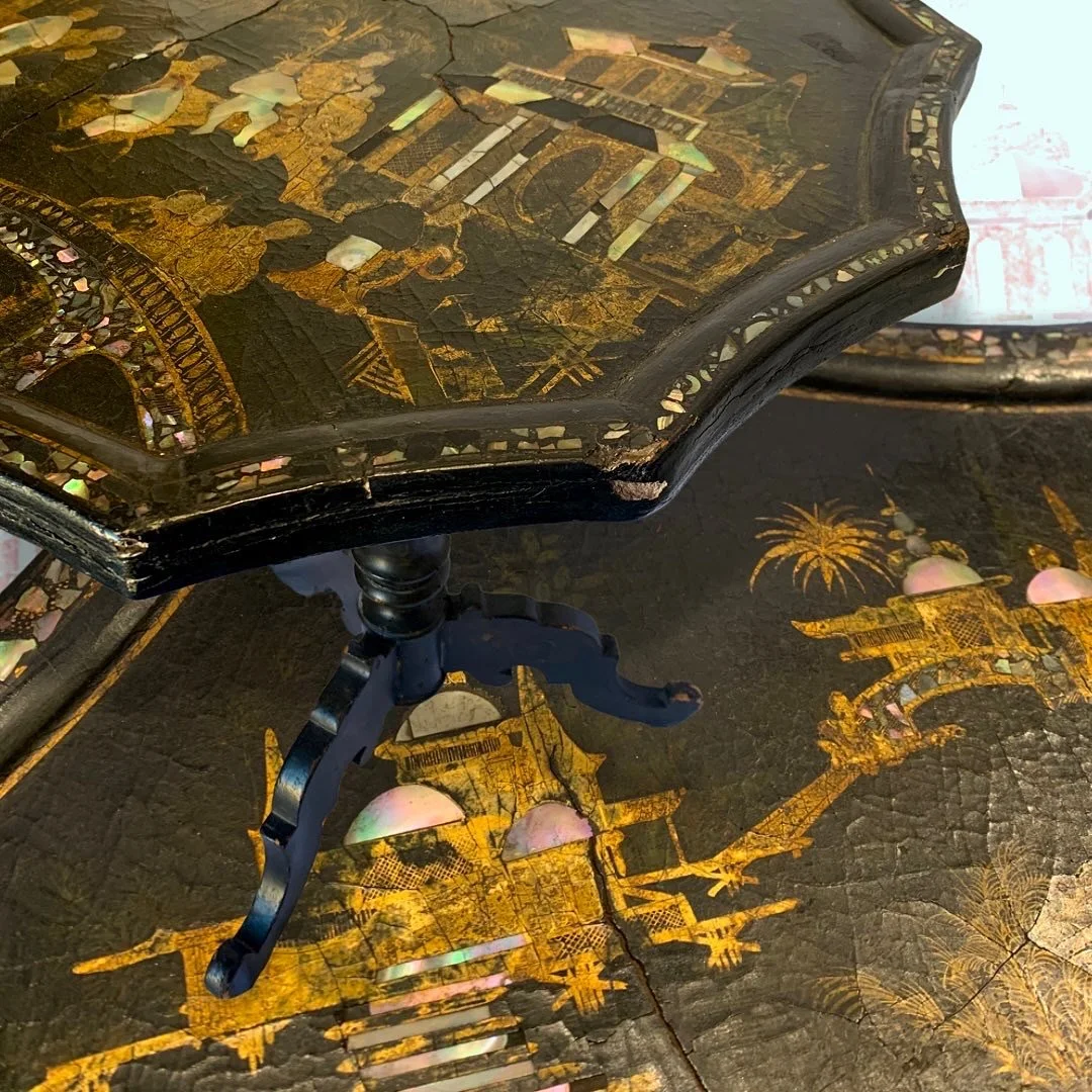 Close-up of a damaged antique table with intricate gold and mother-of-pearl inlay, showing a cracked surface and a chipped edge.