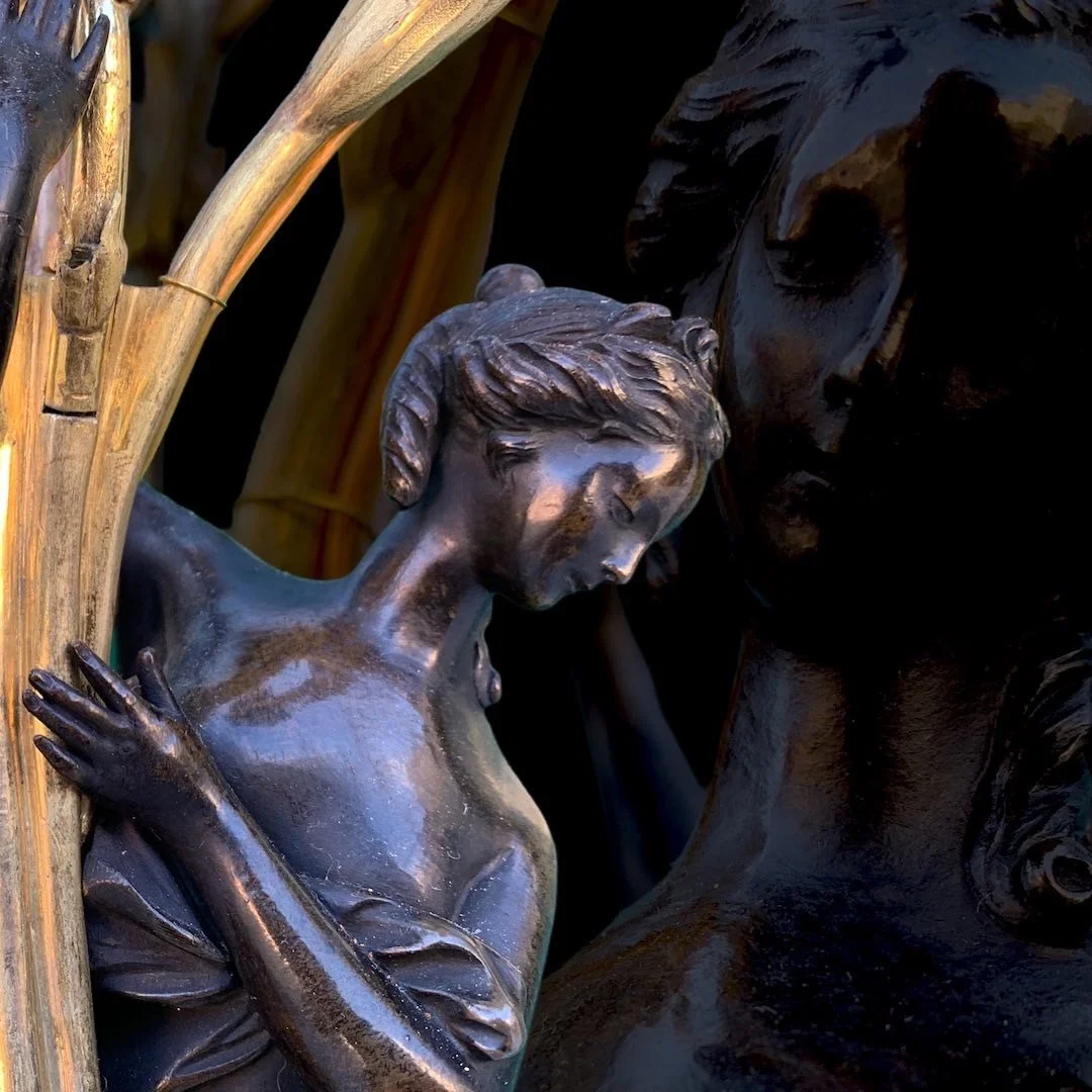 Close-up of bronze sculptures depicting a woman and a man in an intimate pose, with a wooden structure and bamboo in the background.