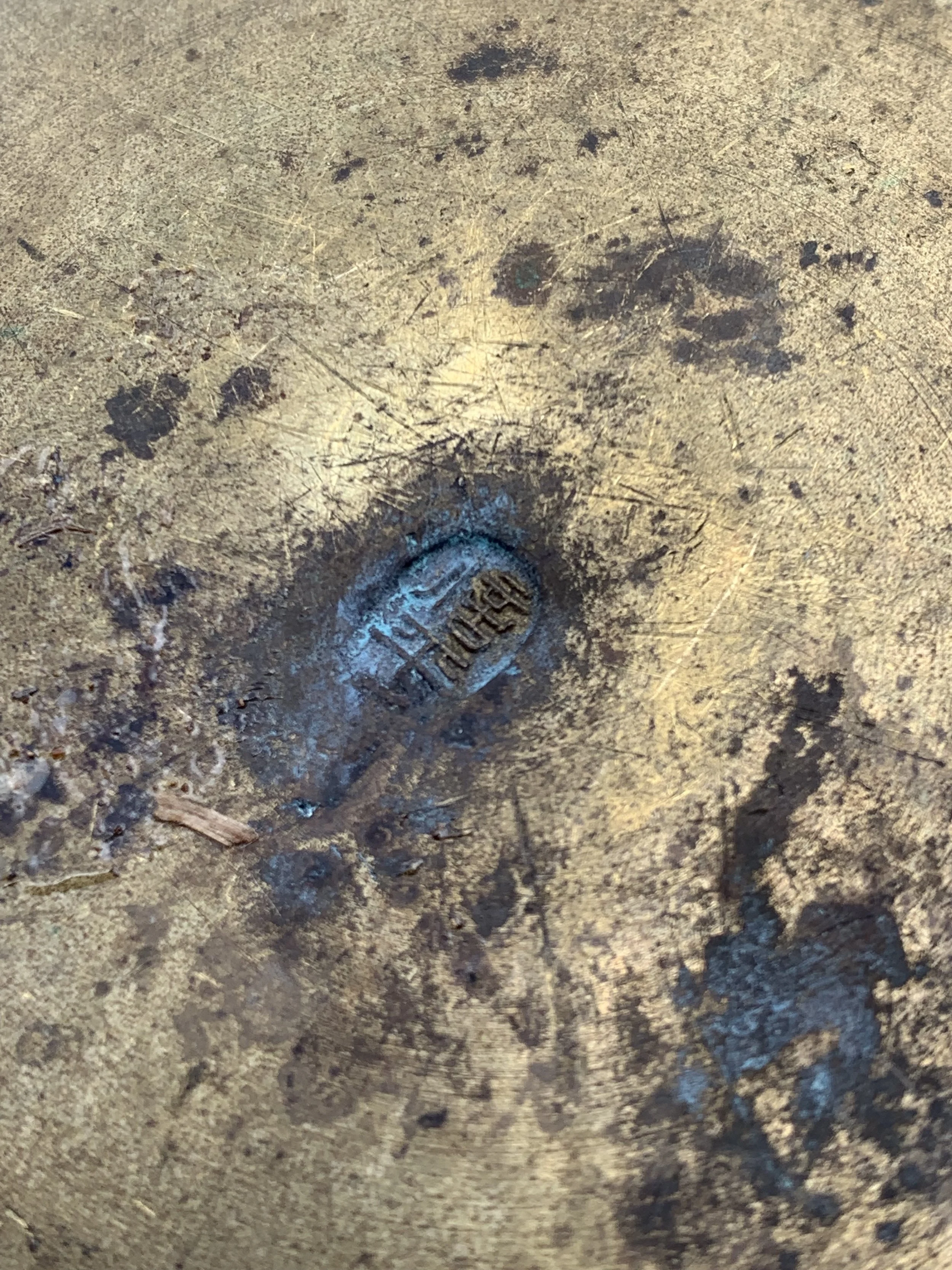 Close-up of a weathered metallic surface with a small, oval-shaped, engraved mark or stamp in the center.