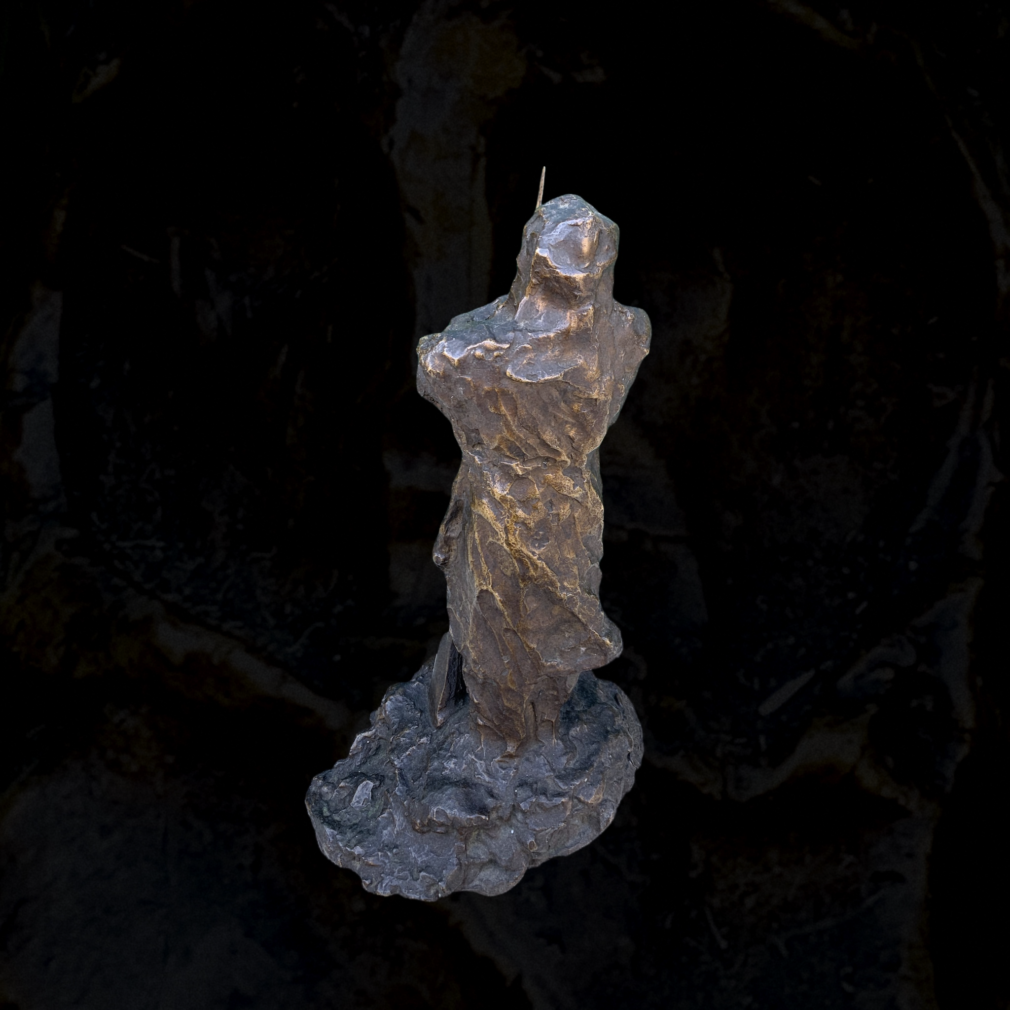 Close-up of a rough, metallic, irregularly shaped sculpture or rock against a dark background.