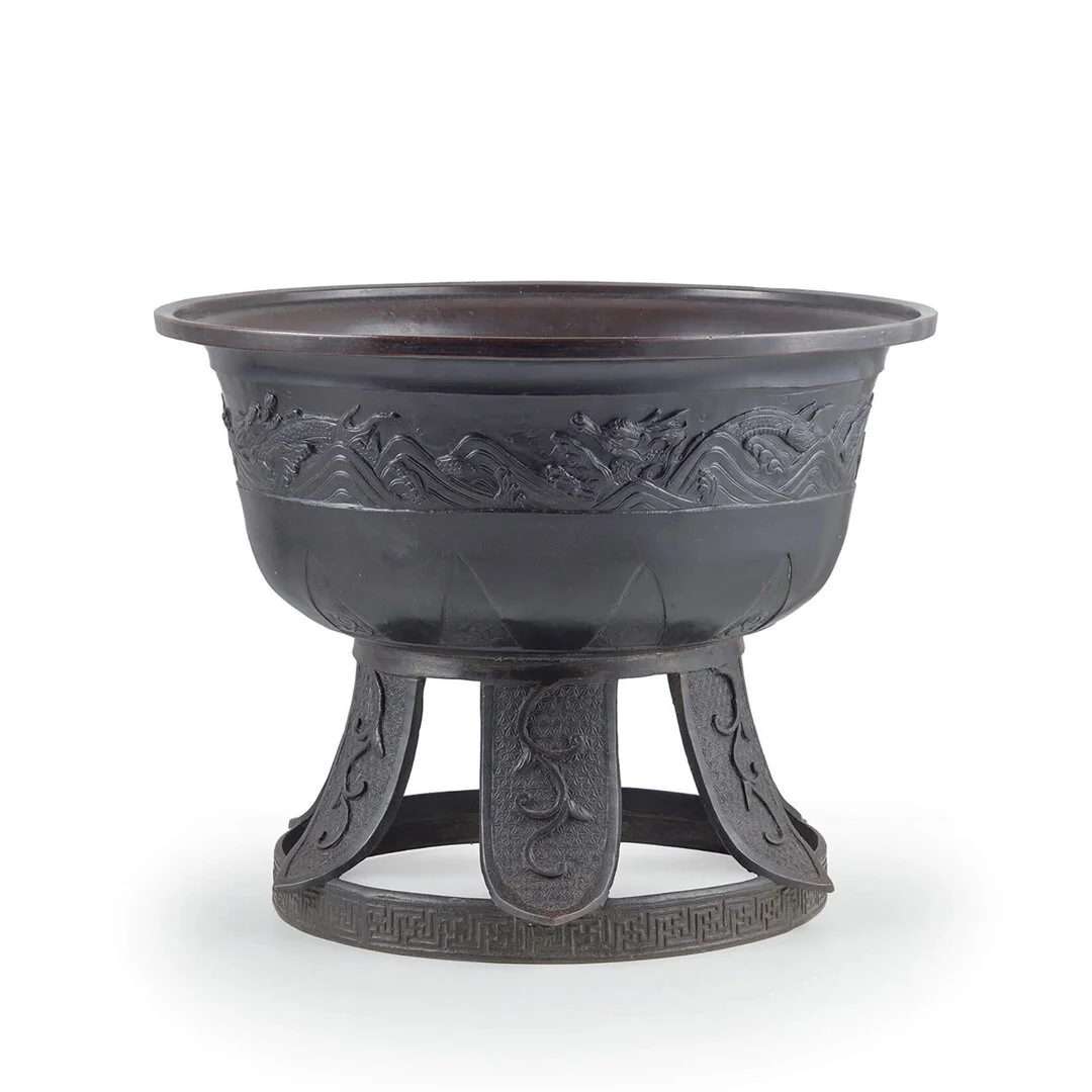 Black antique bronze vessel with intricate carvings, mounted on a three-legged stand, used for ceremonial or decorative purposes.