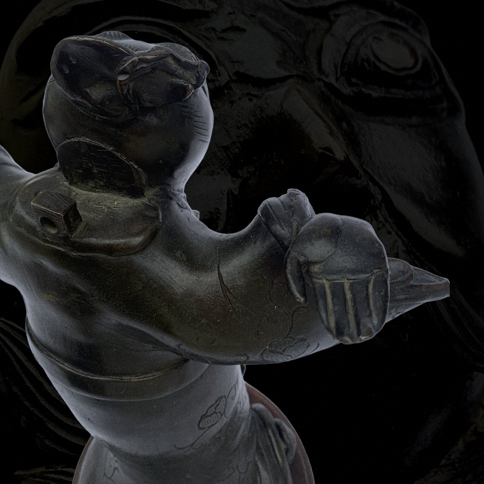 A close-up of a black glass or ceramic figurine depicting a woman with hands raised, wearing a hat, in a glossy finish.