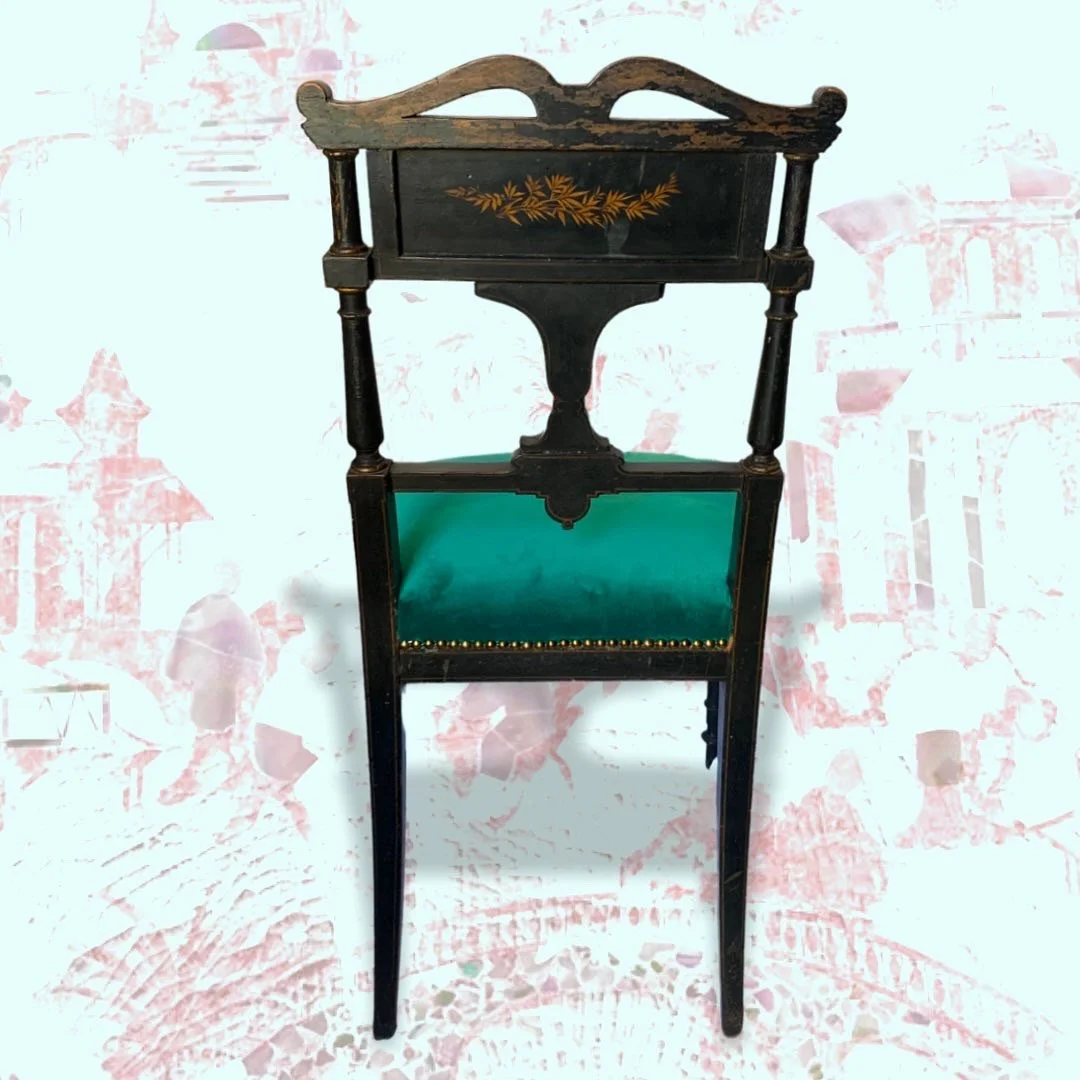 A vintage black wooden chair with a painted floral design on the back panel and a green upholstered seat.