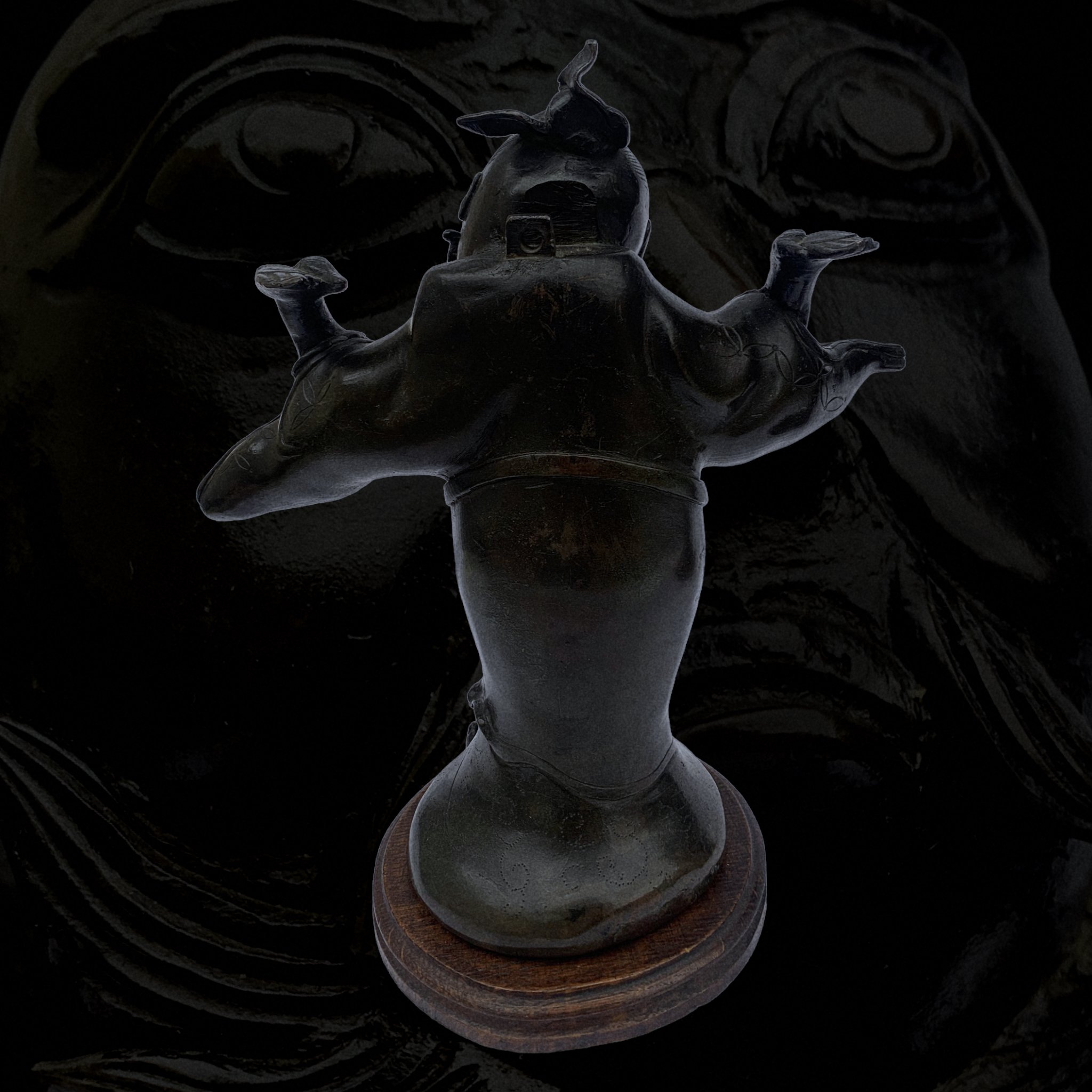 A small figurine of a woman with outstretched arms, made of dark material, placed on a round wooden base.