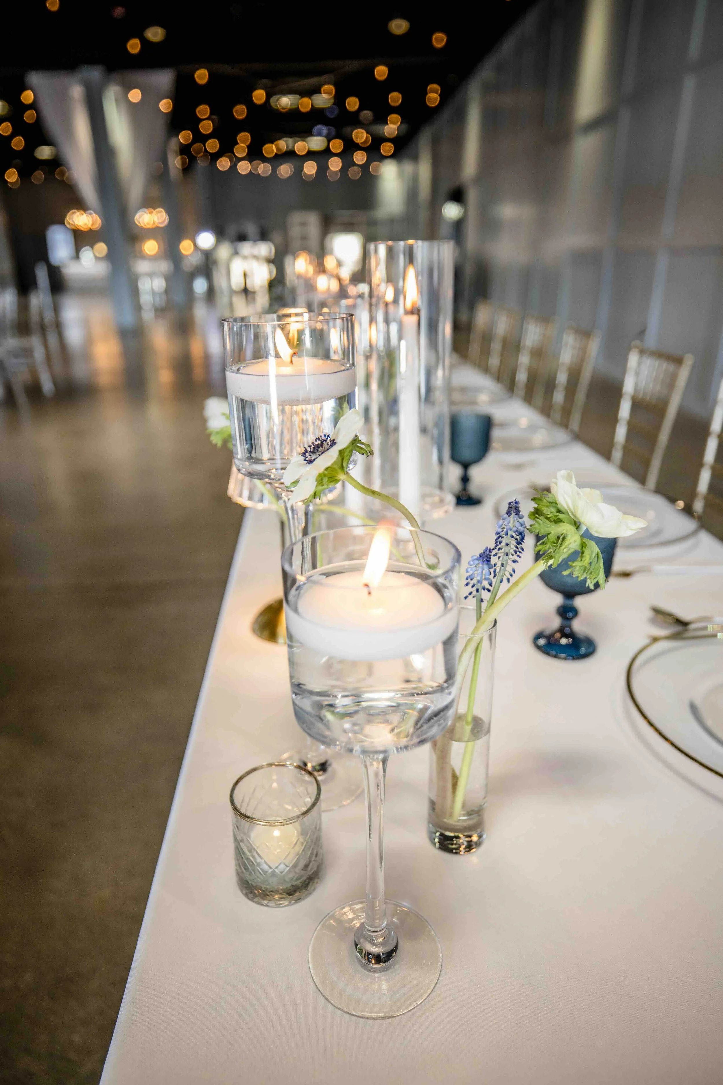 Elegant dining table with floating candles and floral centerpieces at a softly lit event venue.