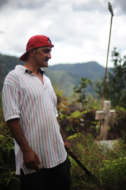  A resident of the mountainous region of Lares holds a machete used to clear jungle debris stands in front of a tomb memorializing Toño Bicicleta. He is one of the only surviving people who knew of Toños whereabouts during his sixteen years as a fugi