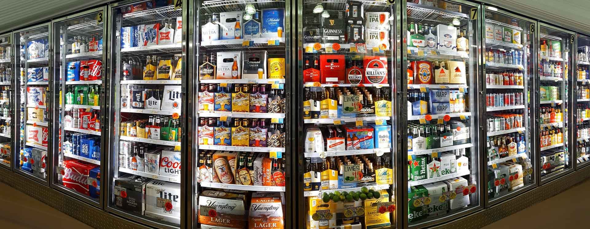 Refrigerators filled with various beverages, including beer, soda, and bottled drinks, in a grocery store aisle.