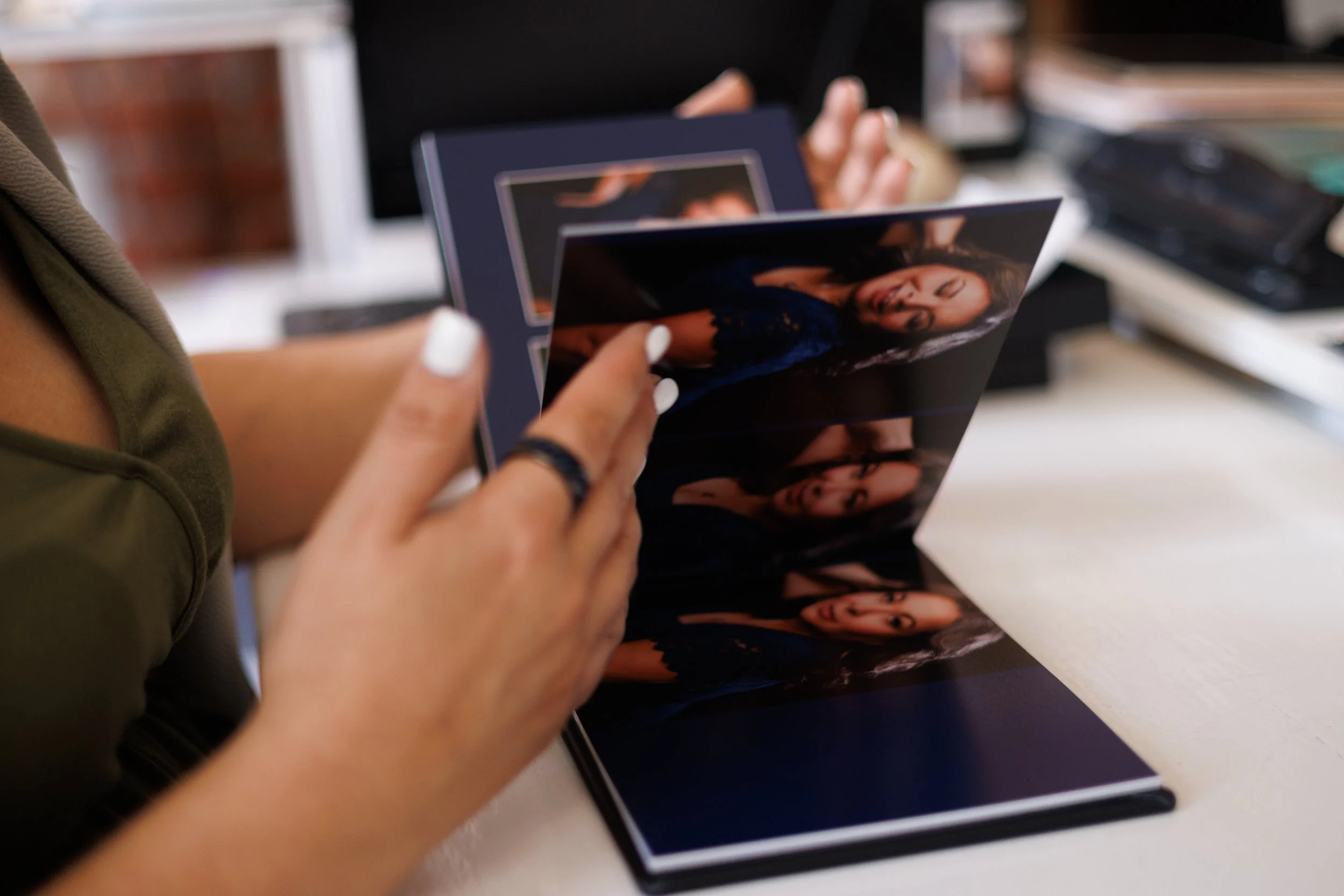 Woman holding fine art matted portrait prints from a luxury photography folio box while reviewing professional portrait photographs at a table.