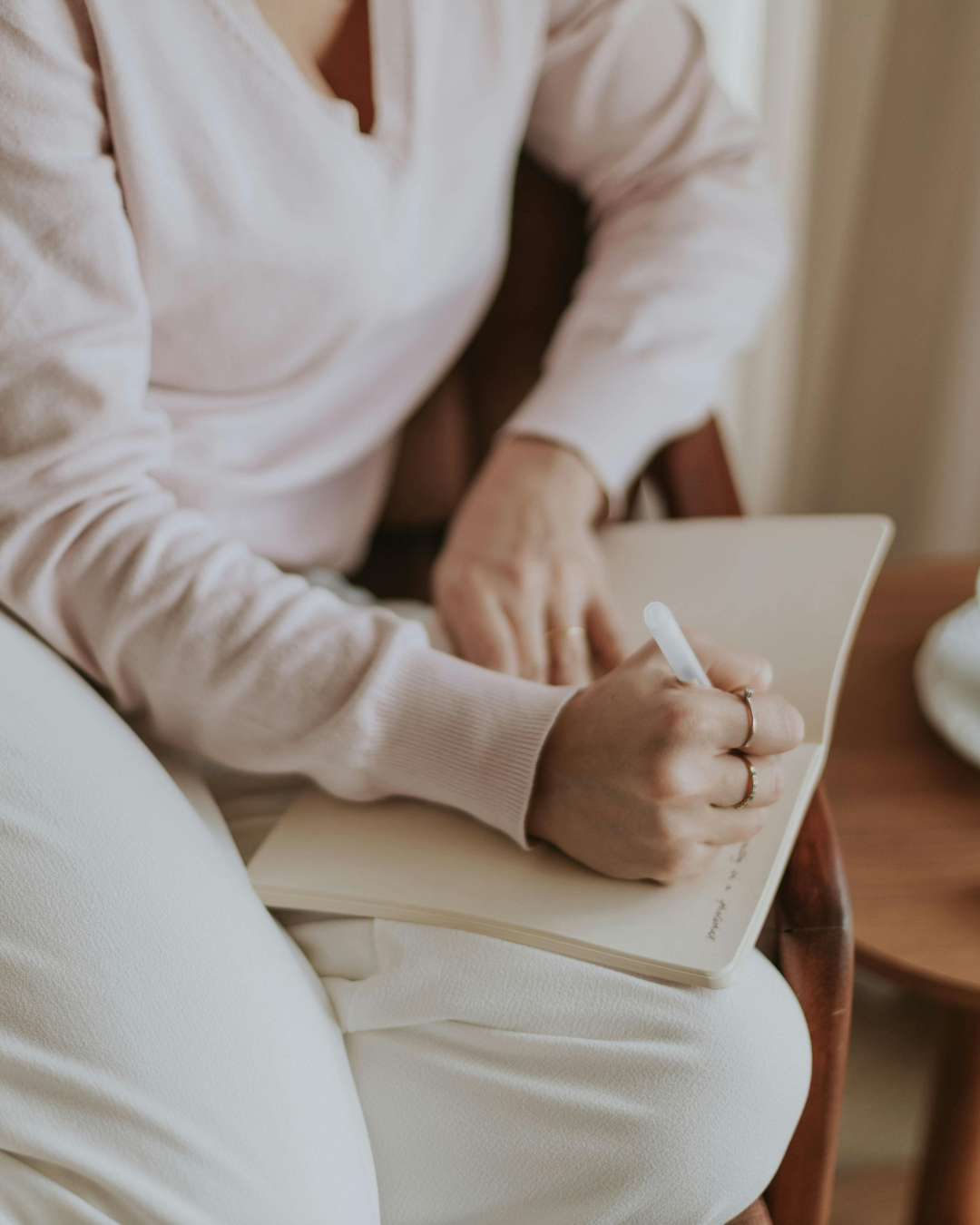 Person wearing a light pink sweater writing in a notebook with a white pen.