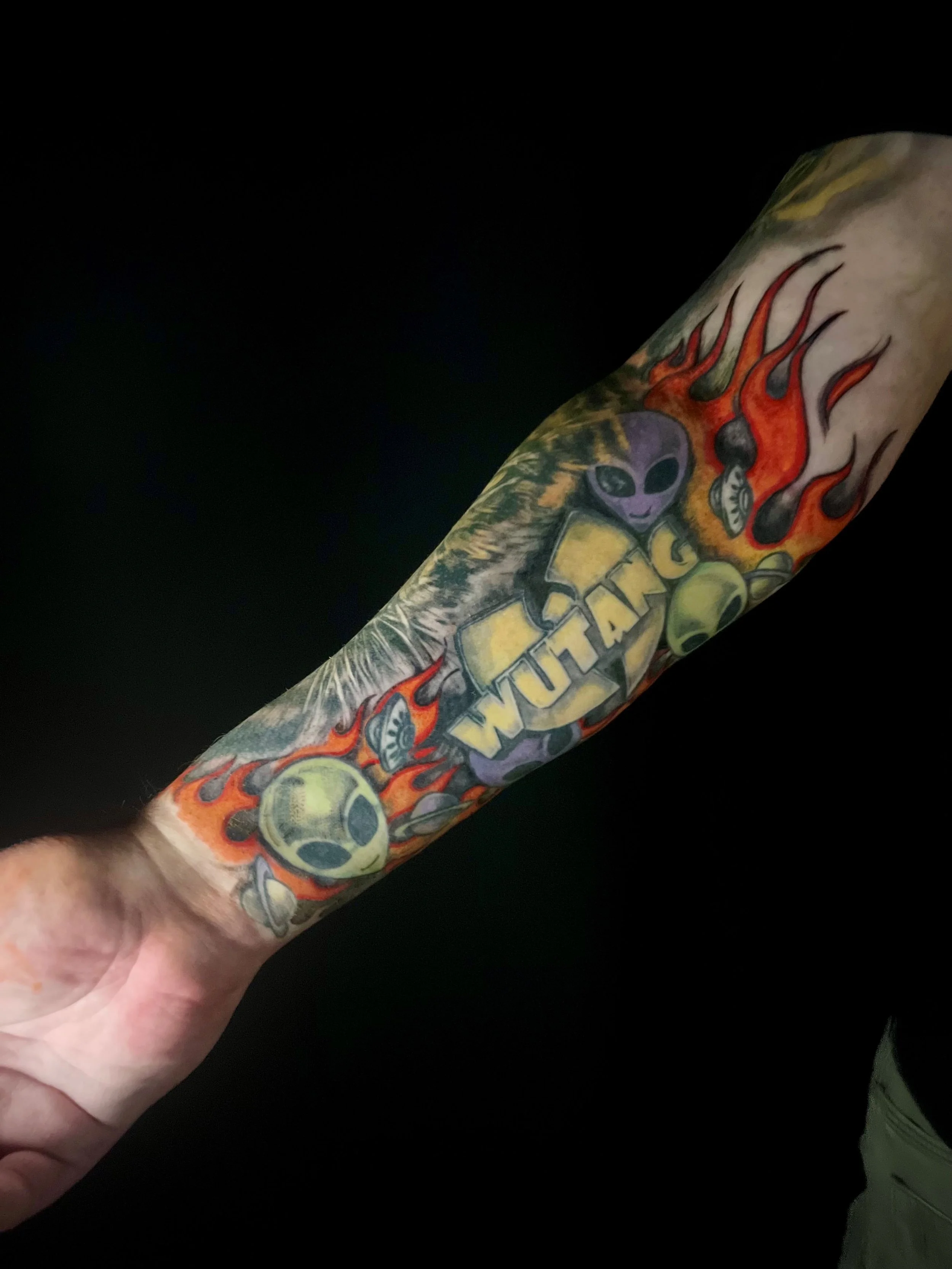 Bold sci-fi forearm tattoo featuring colorful aliens, flames, and a grenade, custom designed at Brass Knuckles Ink Tattoo Studio