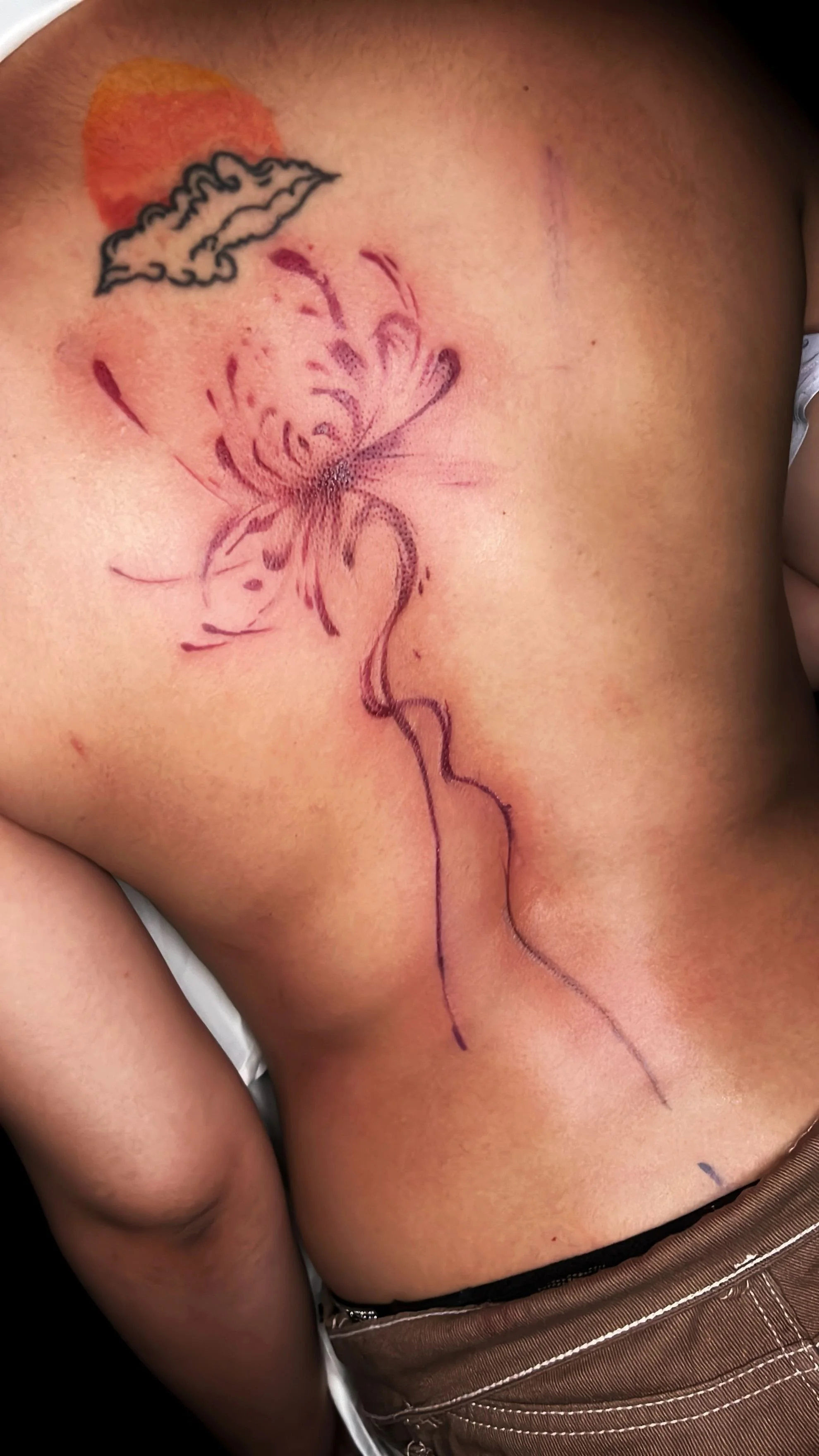 Elegant abstract floral spine tattoo featuring fine line detail and soft red ink flow, custom designed at Brass Knuckles Ink Tattoo Studio.