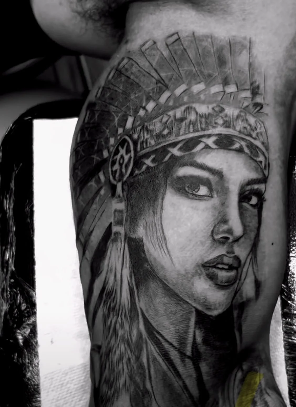 black and grey realism portrait tattoo of woman wearing Native American feather headdress on arm at Brass Knuckles Ink Tattoo Studio Bronx, NYC