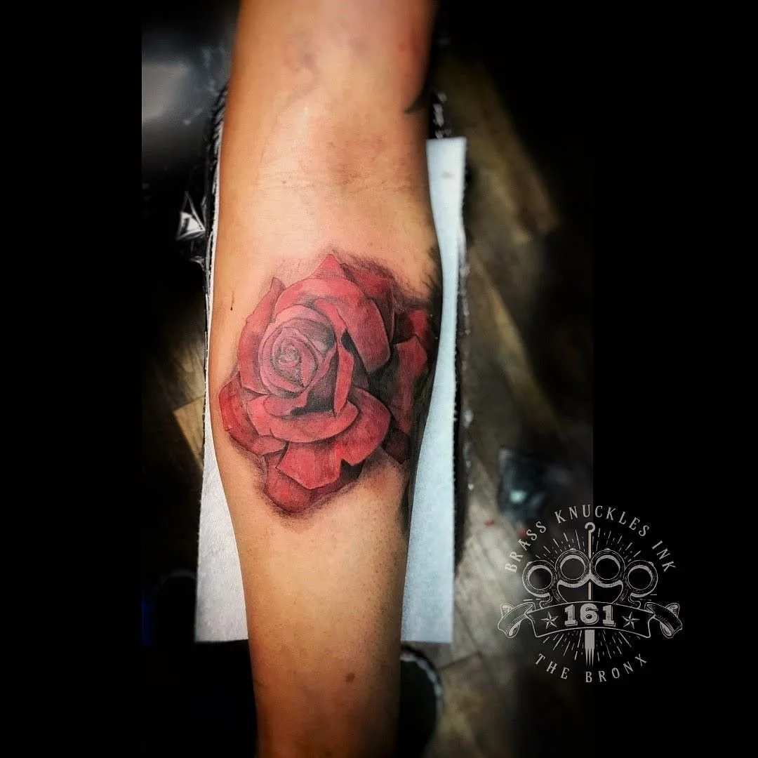 Custom realistic red rose forearm tattoo featuring soft black and grey shading with vibrant red detail, created at Brass Knuckles Ink Tattoo Studio.