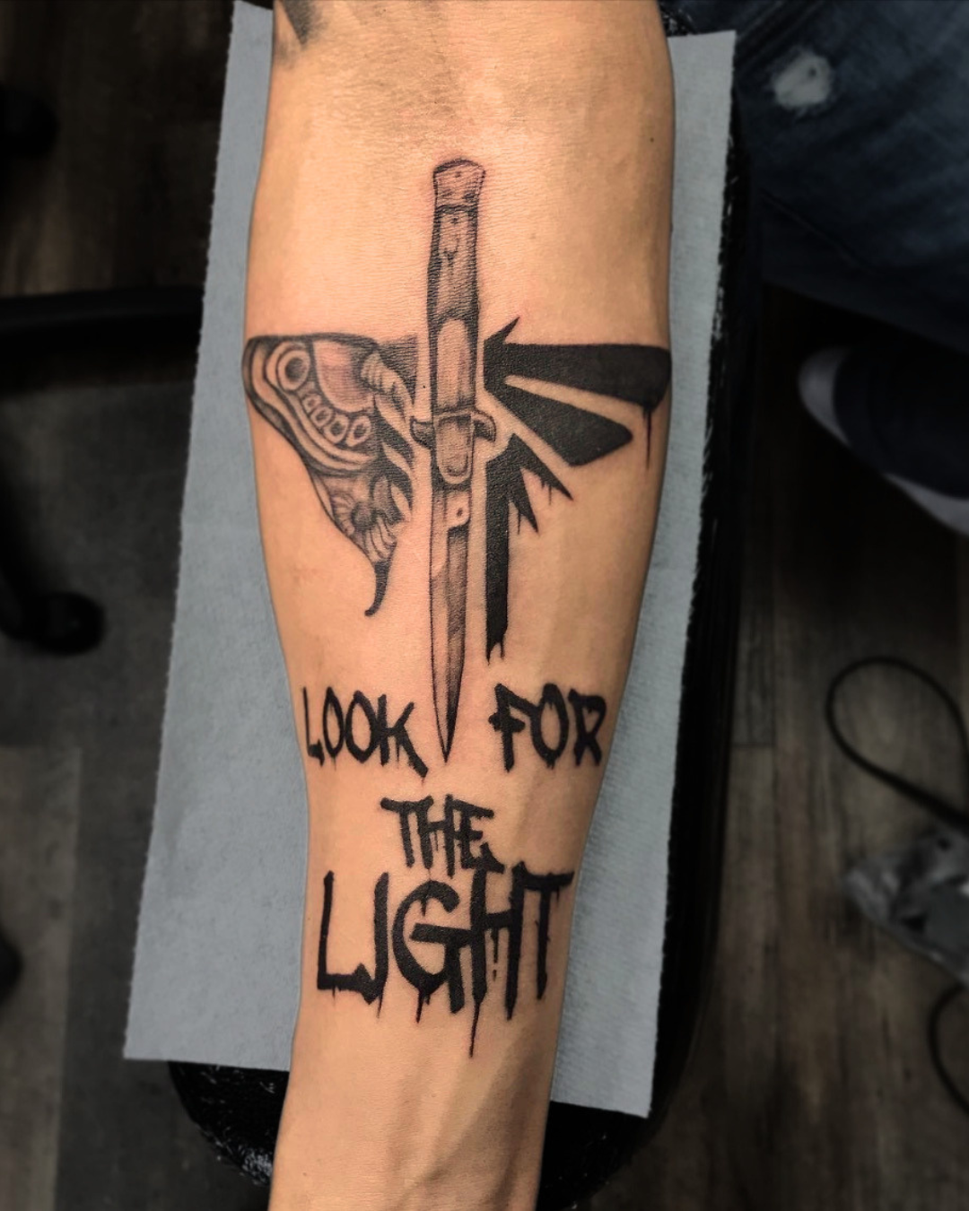 Custom forearm tattoo featuring butterfly, dagger, and ‘Look for the Light’ lettering by Brass Knuckles Ink
