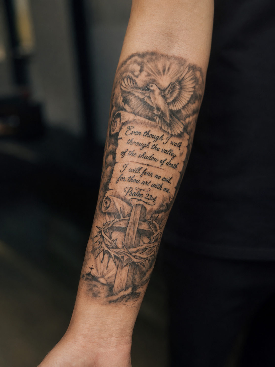 Black and grey Christian forearm tattoo featuring Psalm 23:4 scripture, a dove, cross, and crown of thorns. Custom faith-based tattoo completed at Brass Knuckles Ink Tattoo Studio in the Bronx, NYC