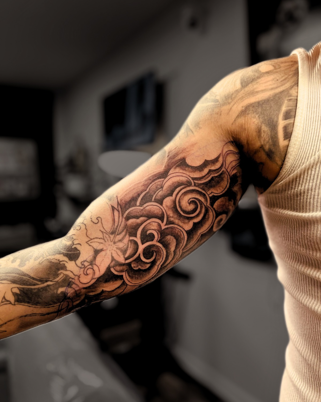 Custom Japanese-inspired black and grey sleeve tattoo featuring traditional wind bars, flowing clouds, and floral elements on the upper arm by Brass Knuckles Ink Tattoo Studio in the Bronx, NY.