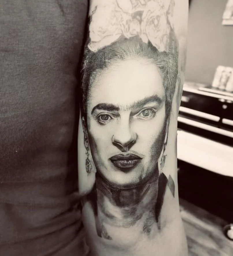 Black and grey realism portrait tattoo  of Frida Kahlo with detailed shading and lifeike features on forearm