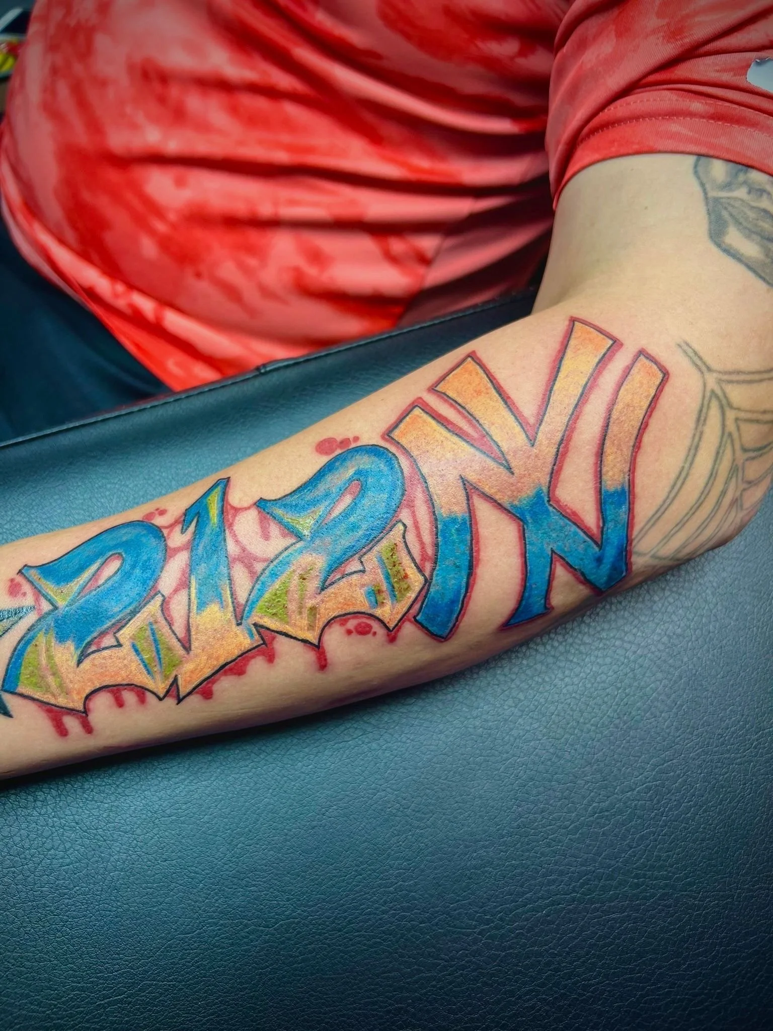 Bold graffiti-inspired "212NY" forearm tattoo featuring vibrant blue and orange tones, custom designed at Brass Knuckles Ink Tattoo Studio