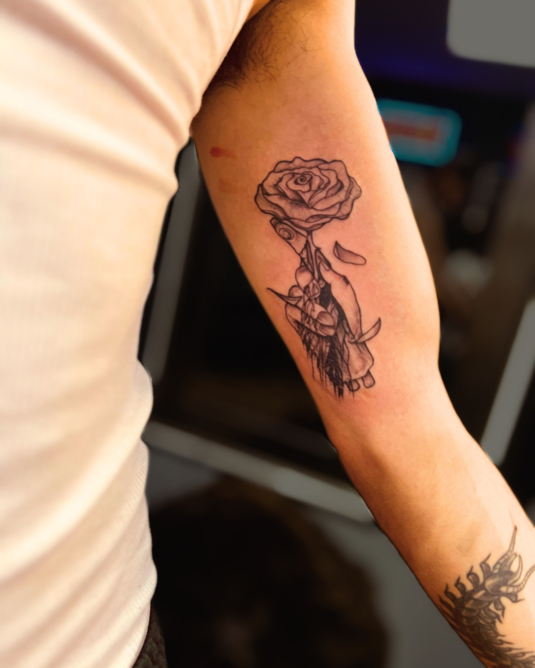 Custom fine line black and grey forearm tattoo featuring a blooming rose transitioning into a detailed skull with falling petals by Brass Knuckles Ink Tattoo Studio in the Bronx, NY.