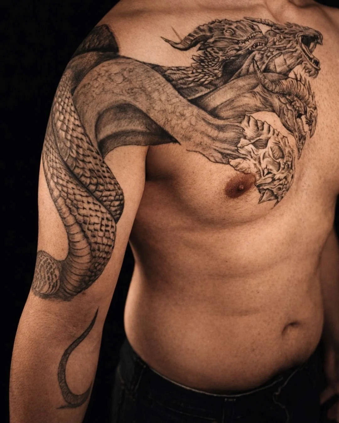 High-detail black and grey realism dragon tattoo spanning chest and arm by Bronx tattoo studio Brass Knuckles Ink