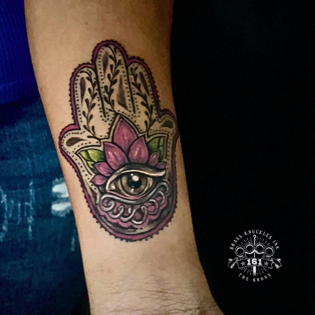 Hamsa hand tattoo with lotus flower and protective eye in ornamental style on forearm at Brass Knuckles Ink Tattoo Studio Bronx NYC